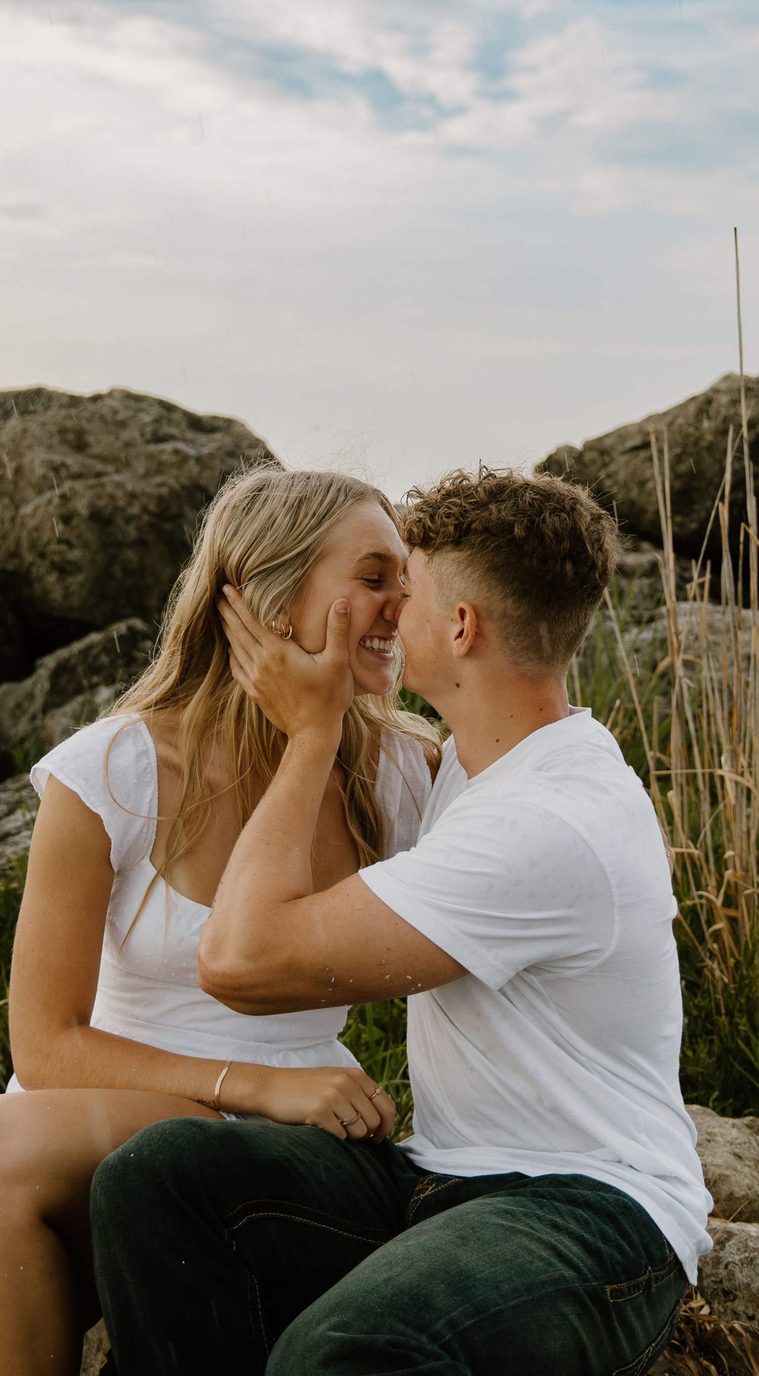 A couple in white shirts share an intimate romantic moment outdoors against a natural backdrop of rocks and tall grass in ohio.