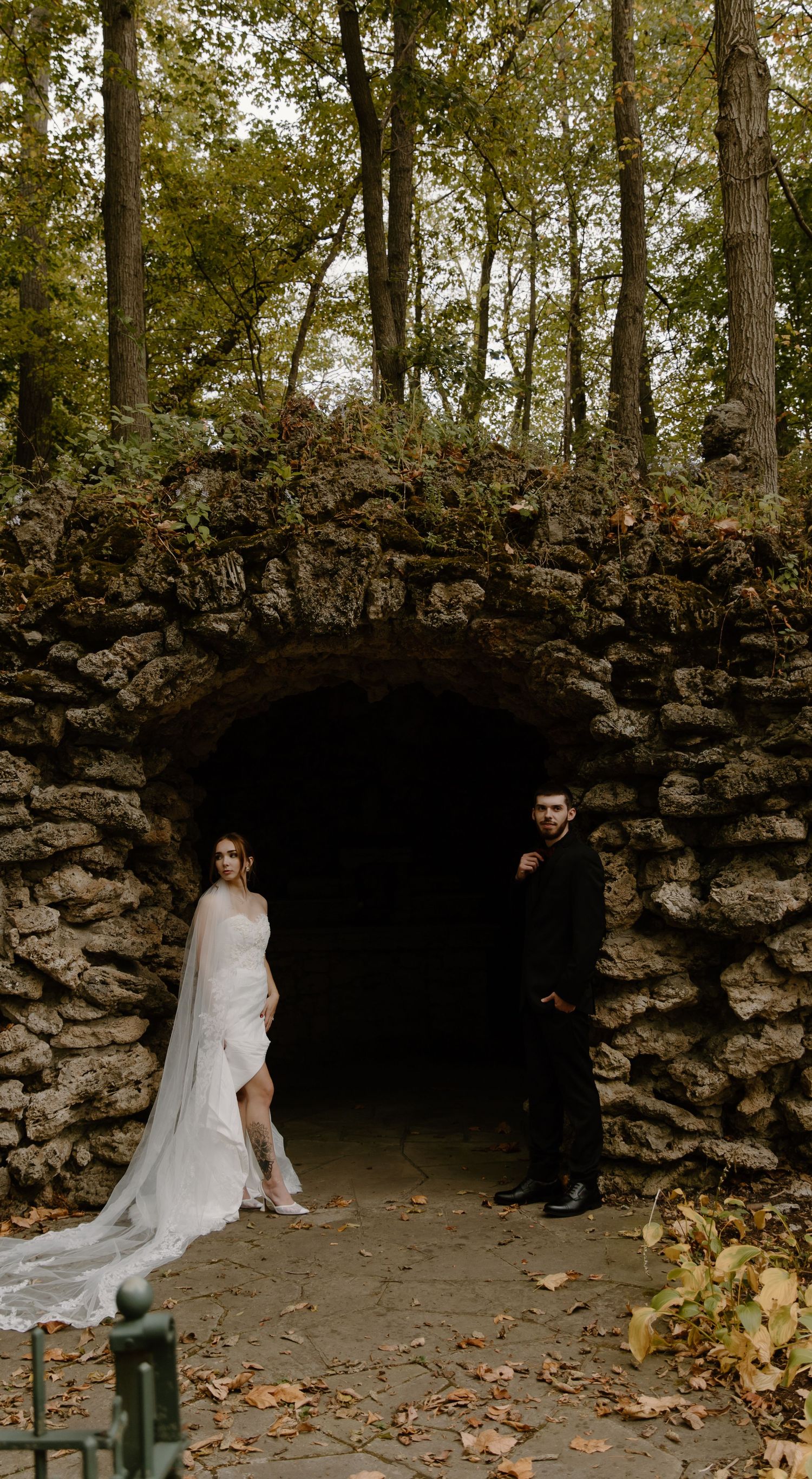 Romantic autumn elopement photo session in a rustic stone grotto with yellow flowers and fallen leaves.