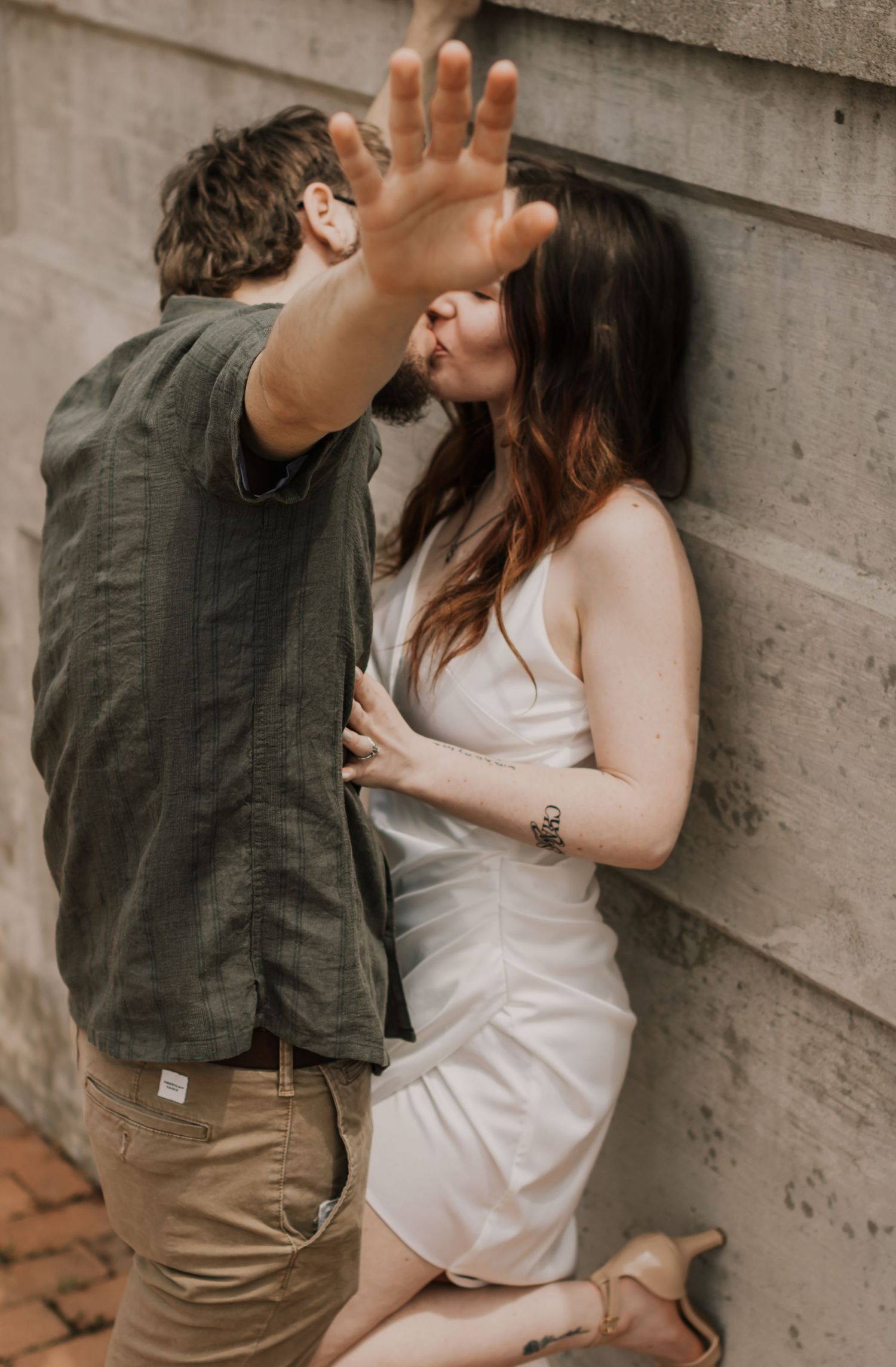 A passionate moment between a couple against a concrete wall in casual summer attire.