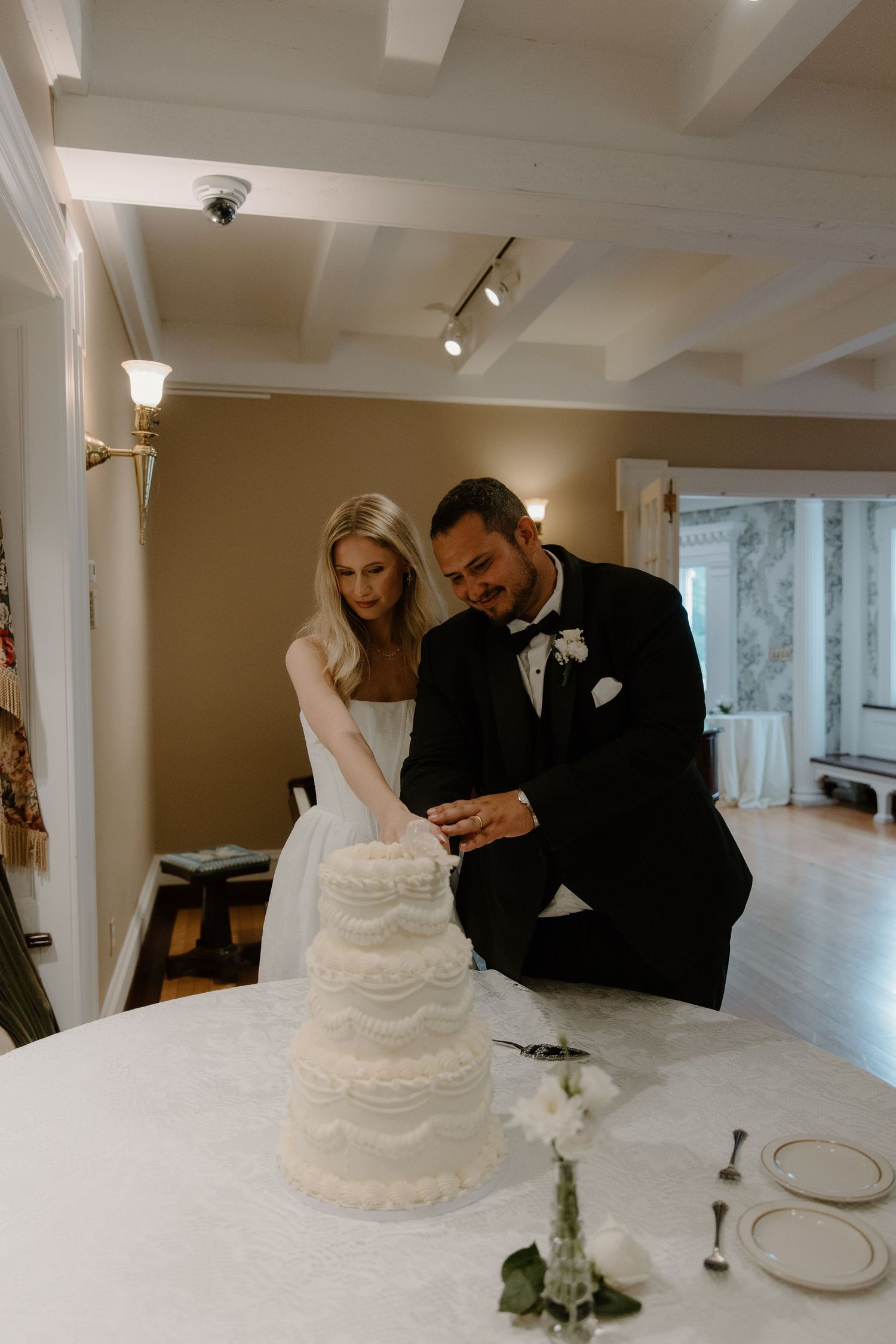 Bride and groom cut their elegant white ruffled wedding cake together in a warmly lit reception room.