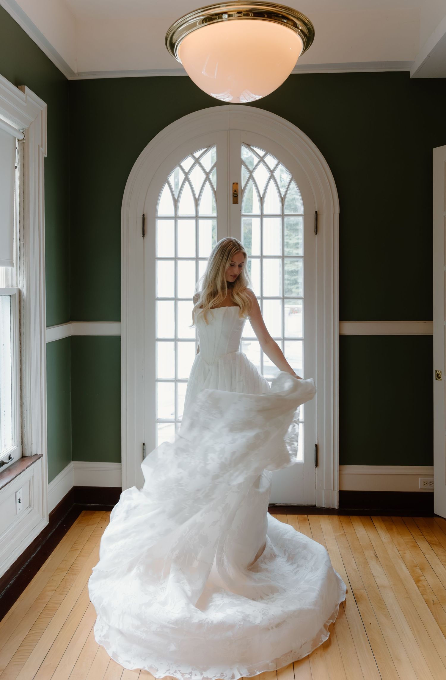 Bride twirls in a stunning layered white wedding gown inside an elegant green-walled room.