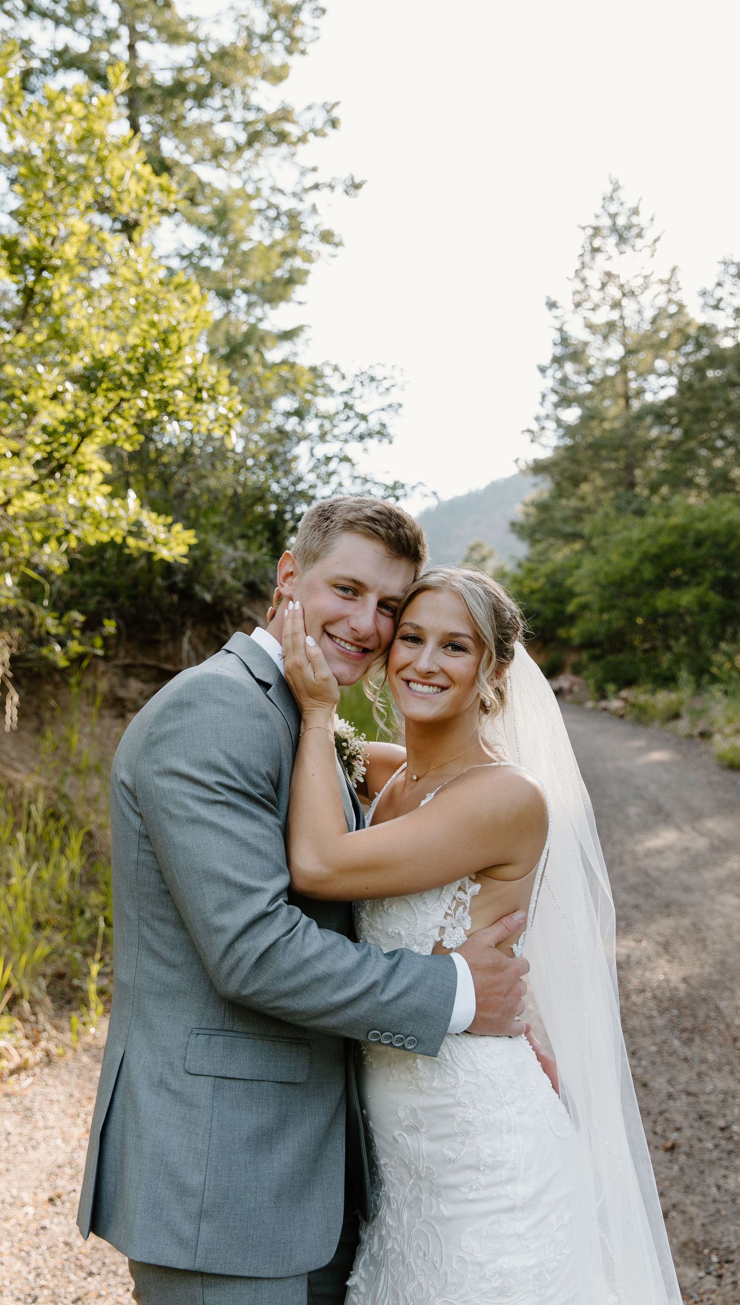 Happy couple embraces on a scenic mountain path during their wedding photoshoot.