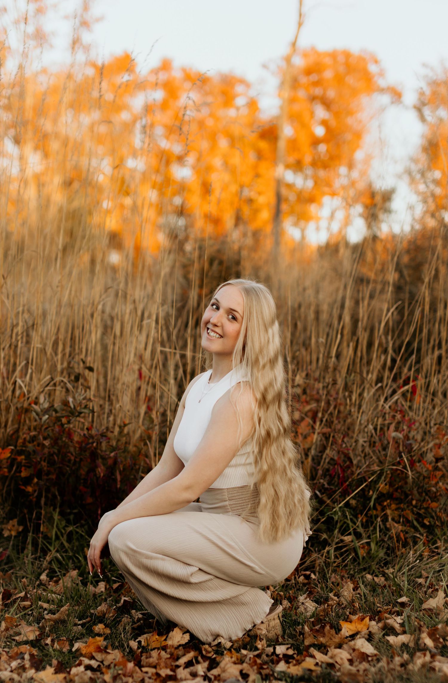 Outdoor portrait amidst tall grass and autumn foliage with warm golden lighting.