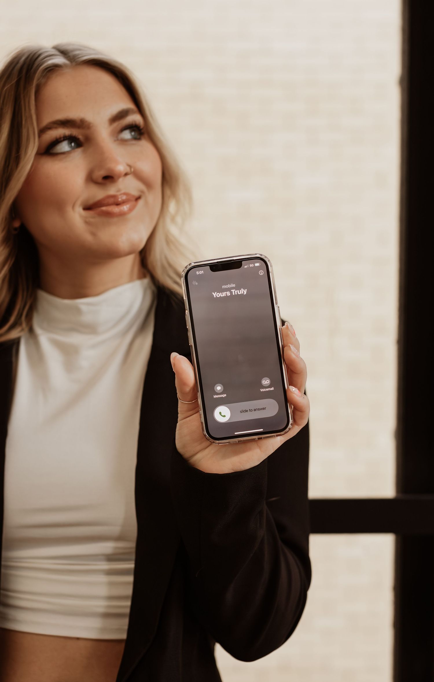 Person in black blazer and white top showing iPhone with screen display.