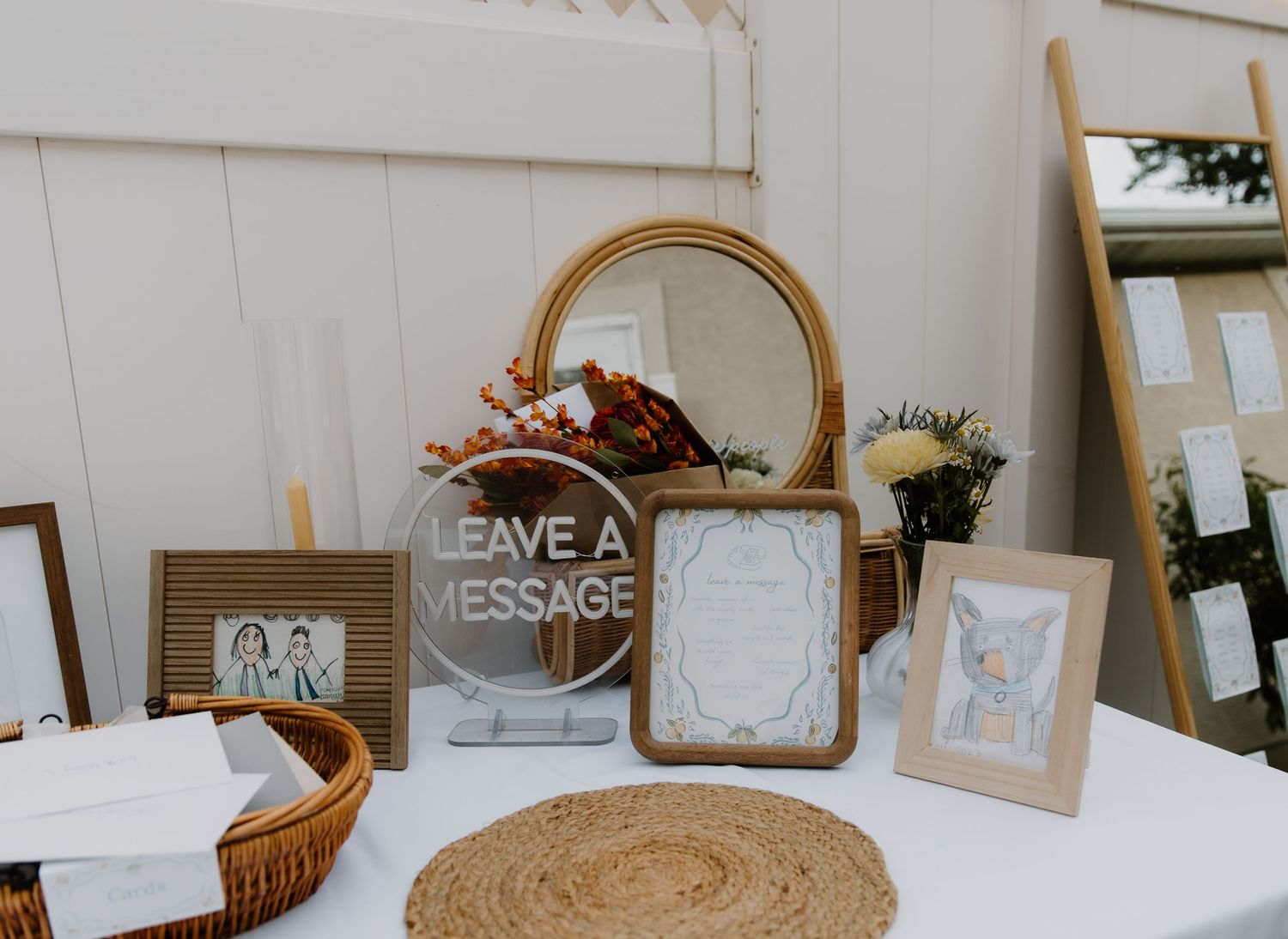 Wedding reception decor table with rustic frames, 'Leave a Message' sign, and decorative elements on white tablecloth.