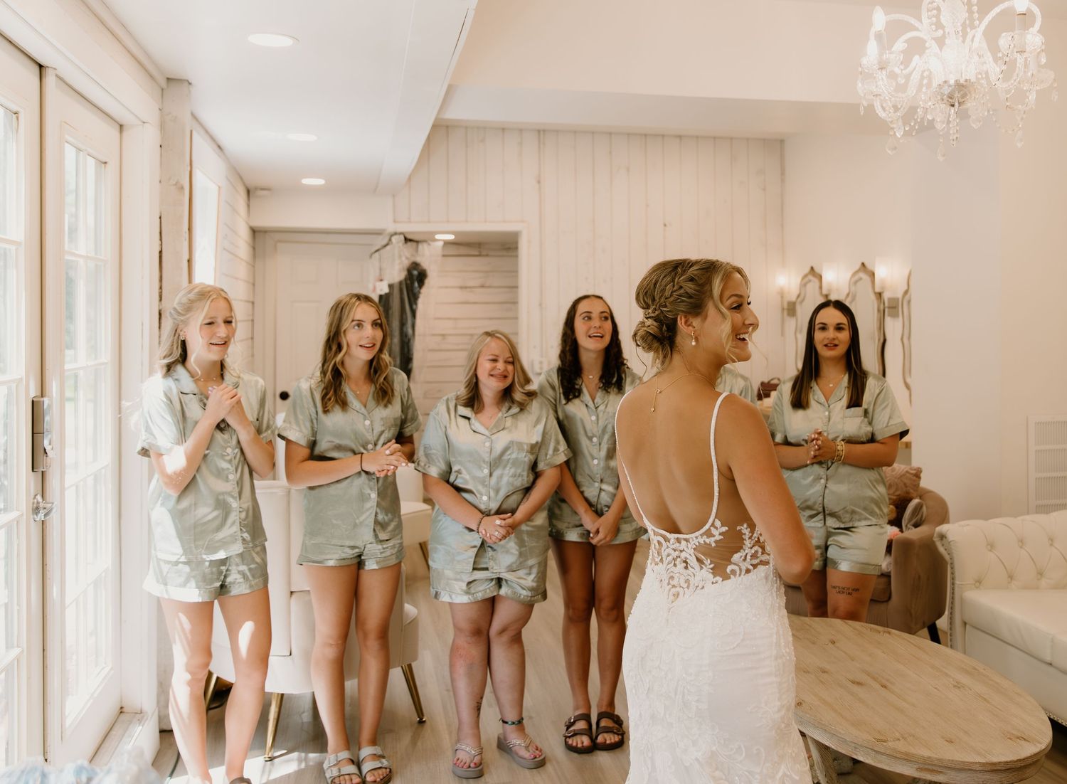 Bridesmaids in light blue dresses gathered in an elegant white room with chandelier.