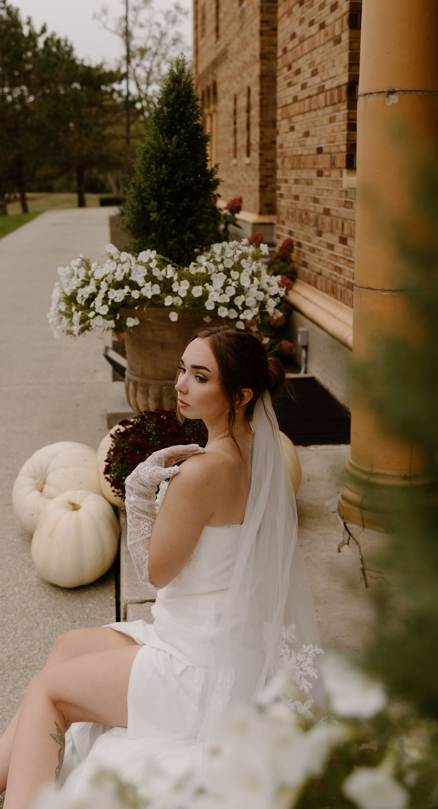 Bride in white wedding dress and veil against Nazareth Hall with autumn decorations and white flowers.