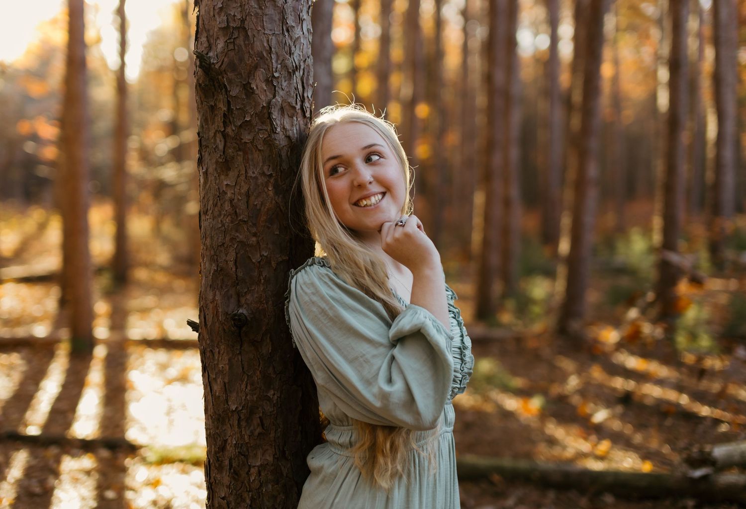 Sunlit forest portrait leaning against tree with golden autumn light filtering through.