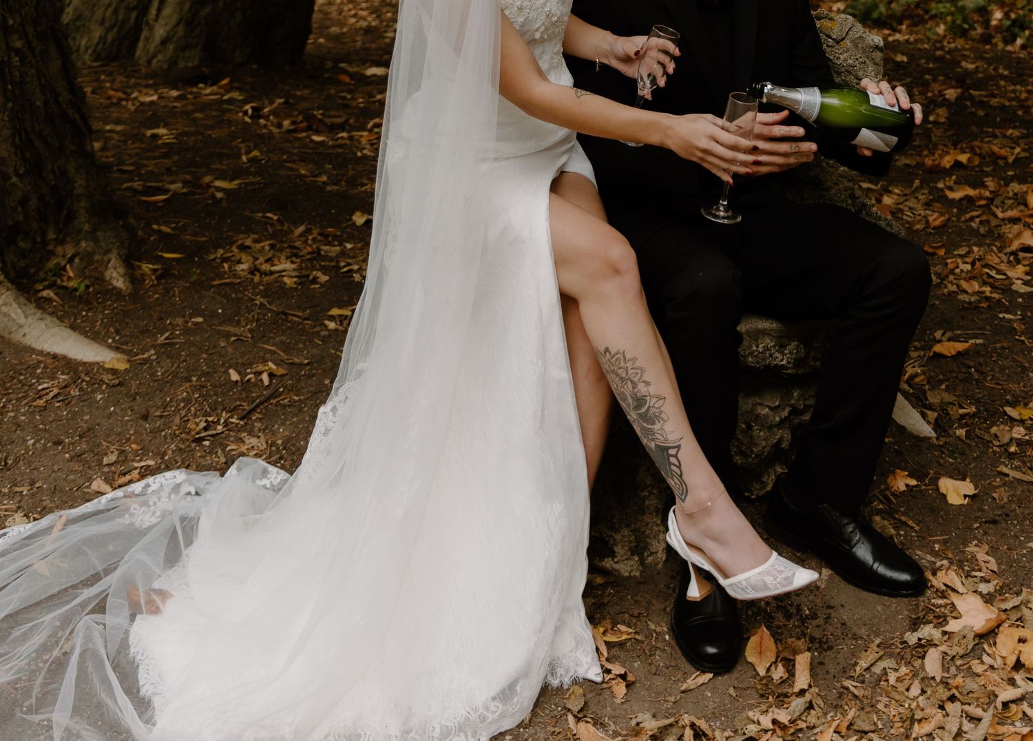 Bride and groom pop champagne while sitting on fallen leaves at Nazareth Hall.
