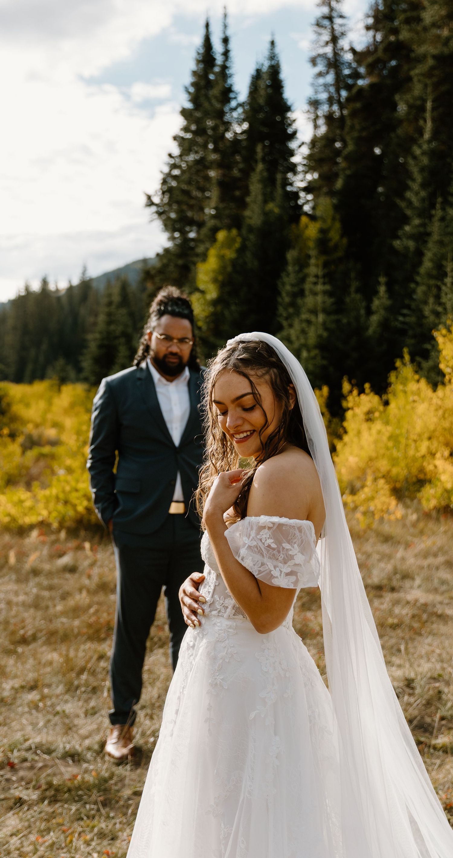 An emotional first look wedding scene set against a backdrop of evergreen trees and mountain peaks.