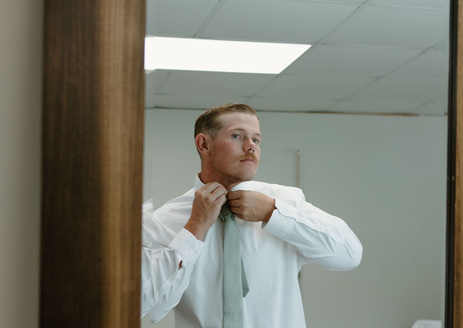 A person in a white button-down shirt sits at a desk in a modern office with reflective glass windows.