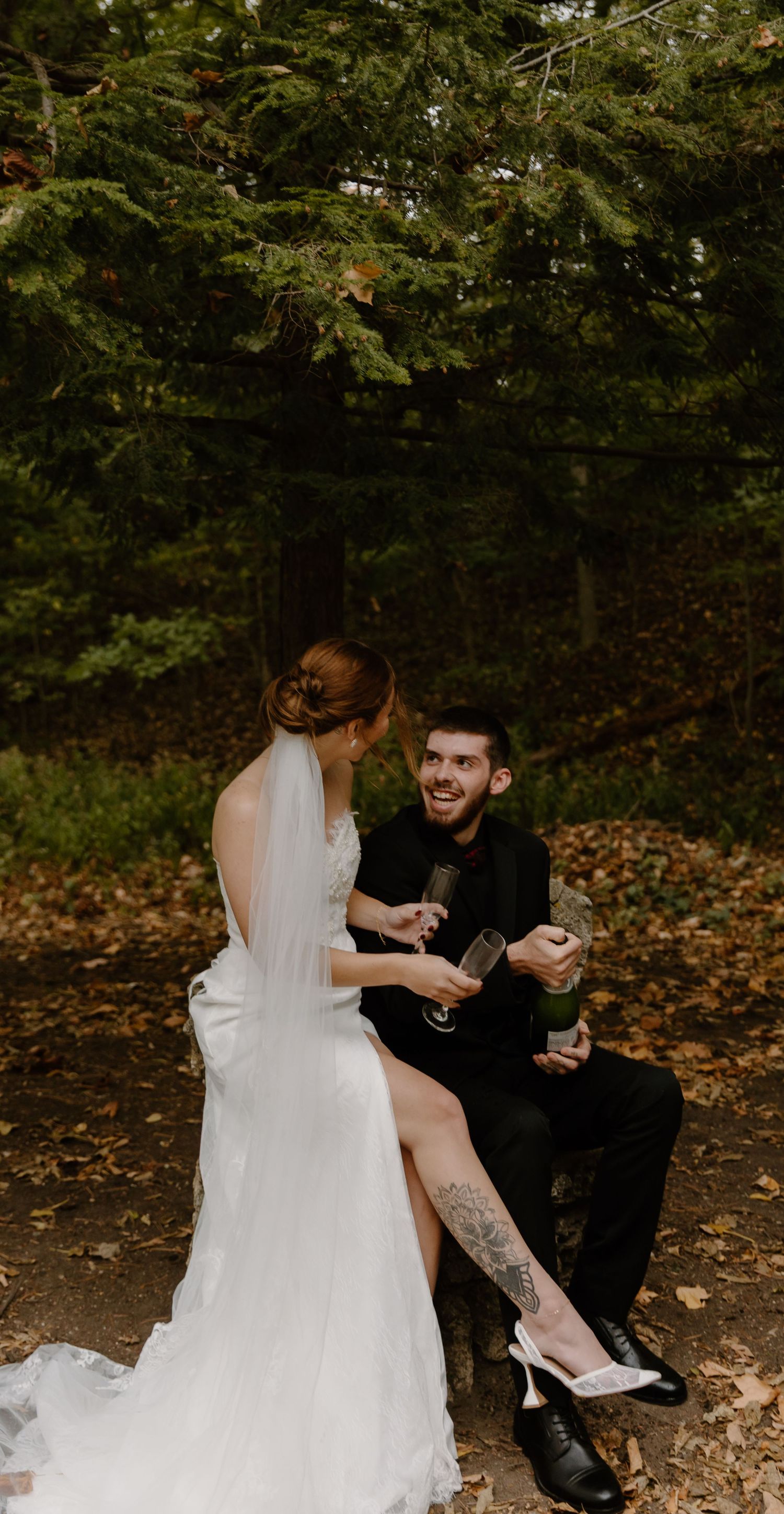A bride and groom share playful moments while sitting among fallen autumn leaves at nazareth hall.