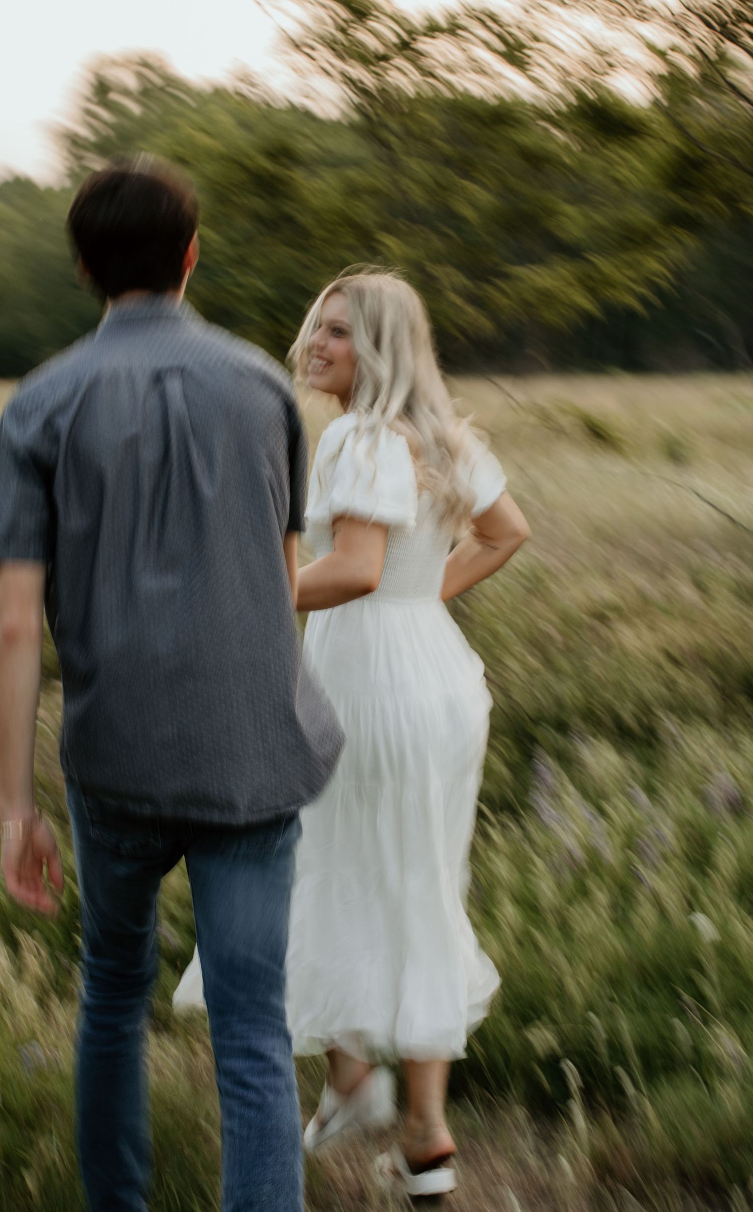 A couple walks through a meadow together during golden hour.