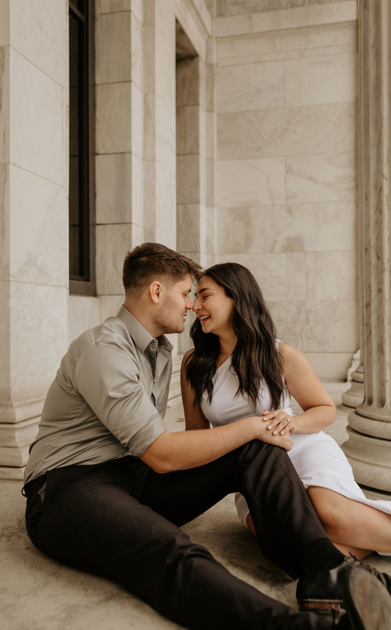 A couple sits intimately on marble steps sharing a tender moment.