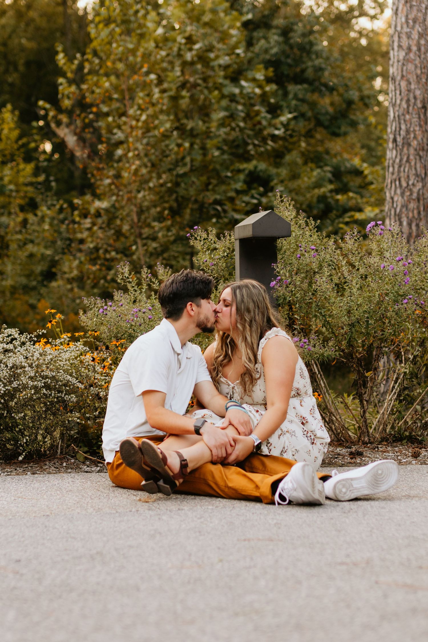 A couple sits close together on a garden path surrounded by greenery.