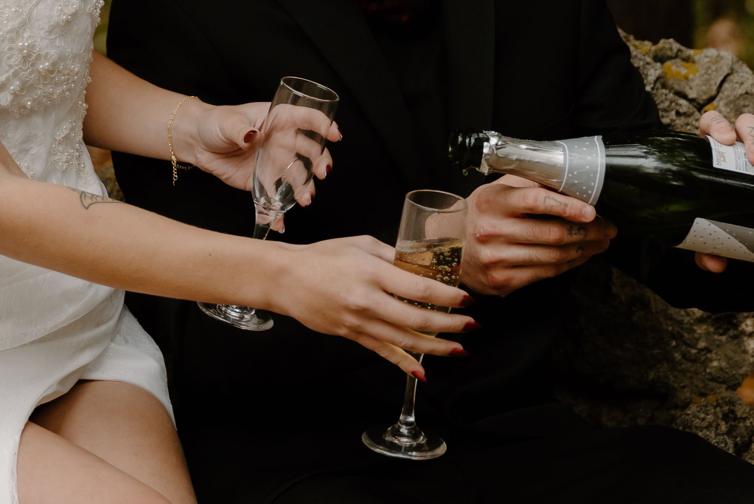 Hands pour champagne into wine glasses during an outdoor celebration.