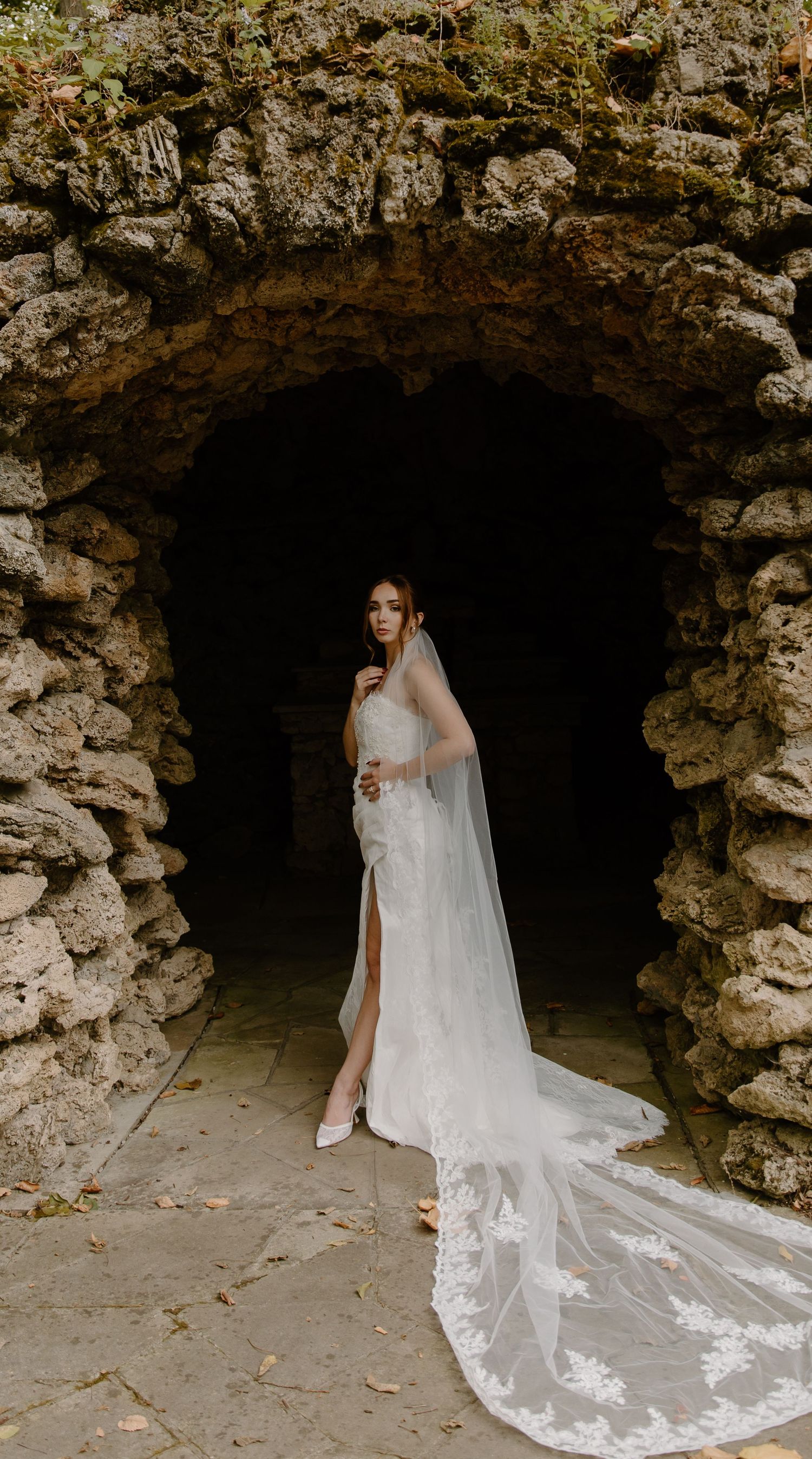 Elegant wedding dress with long flowing veil photographed in a dramatic stone archway cave setting at Nazareth Hall.