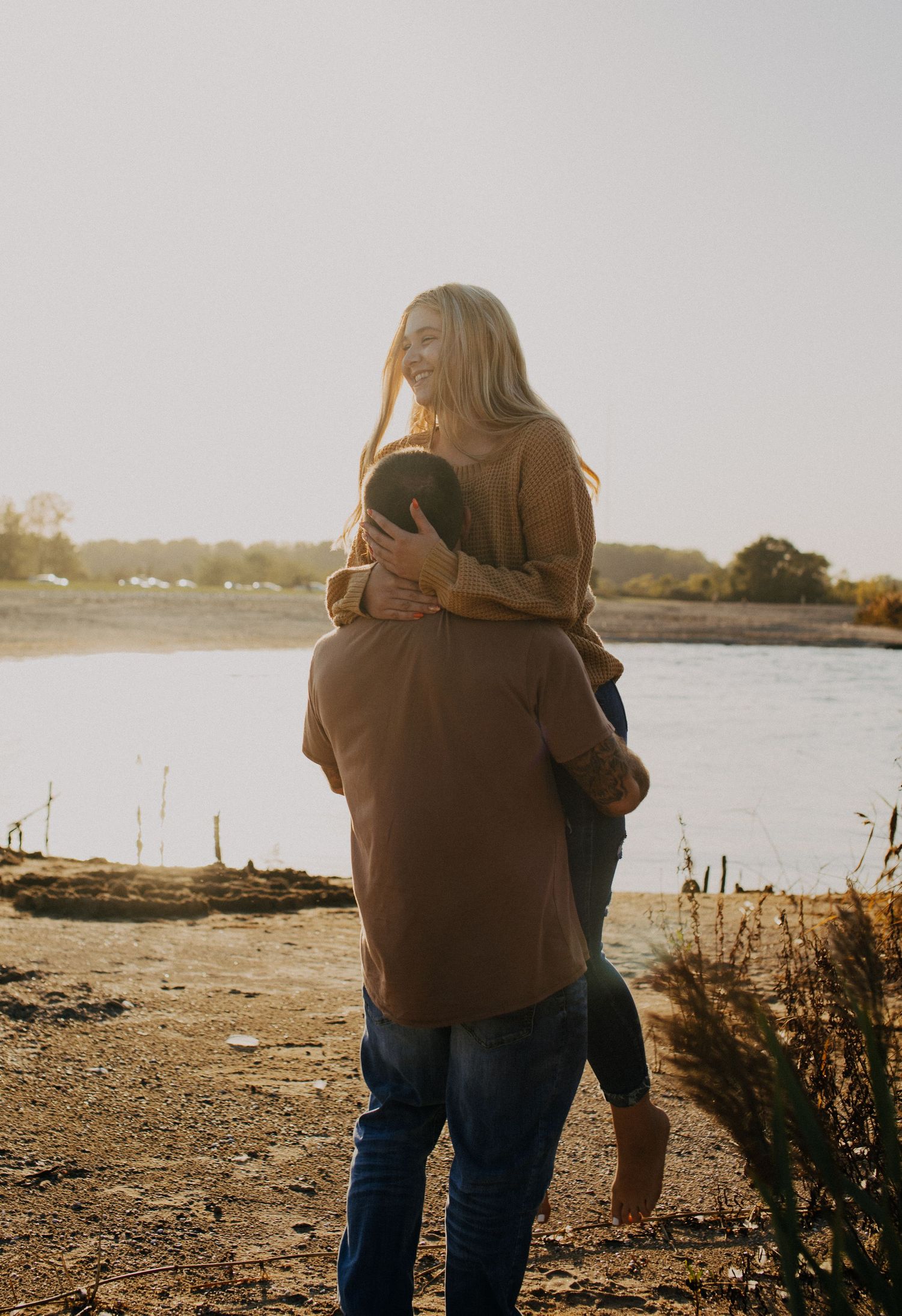 Couple embracing at sunset near a lake with golden light filtering through.