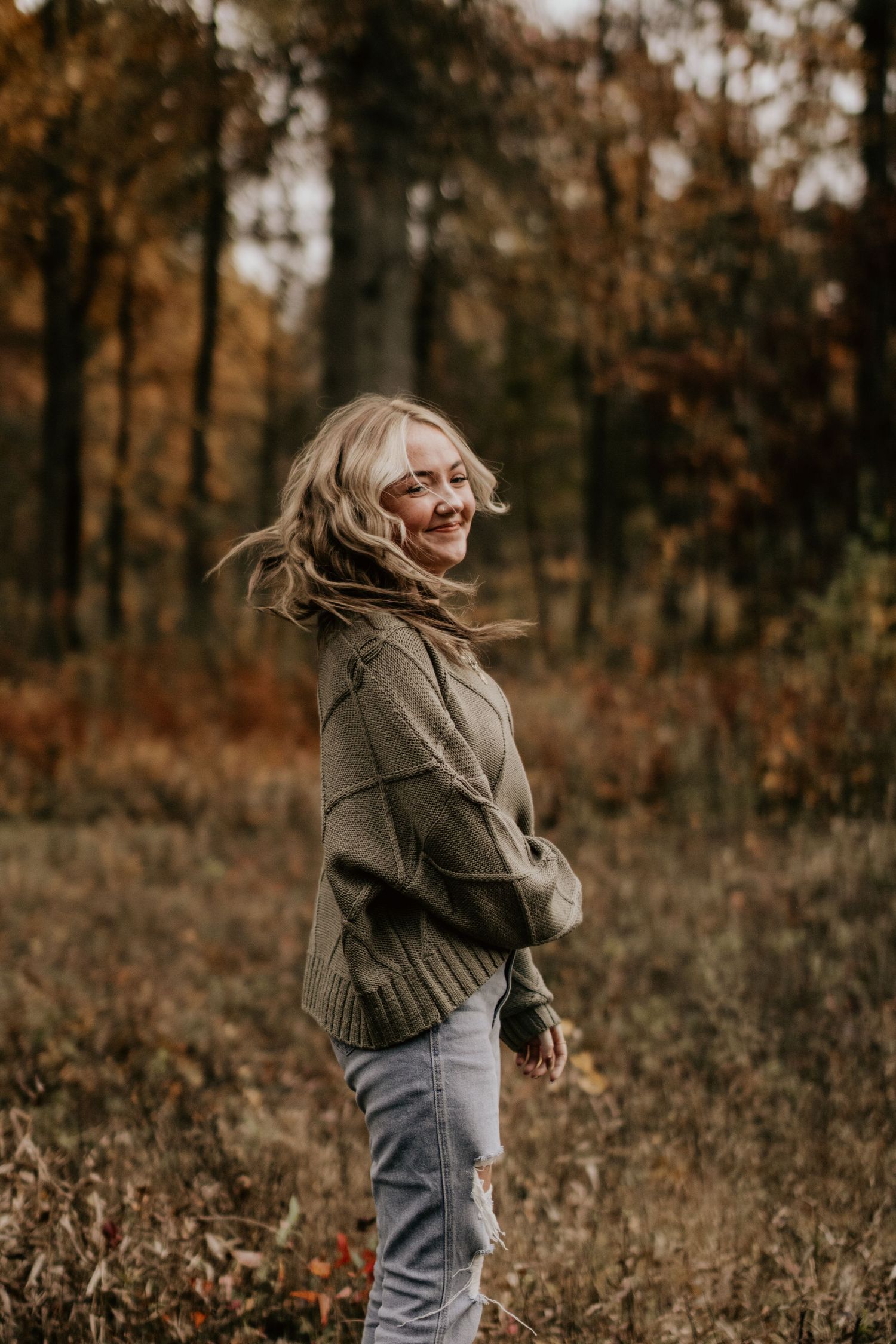 Person in olive sweater spins joyfully among autumn trees.
