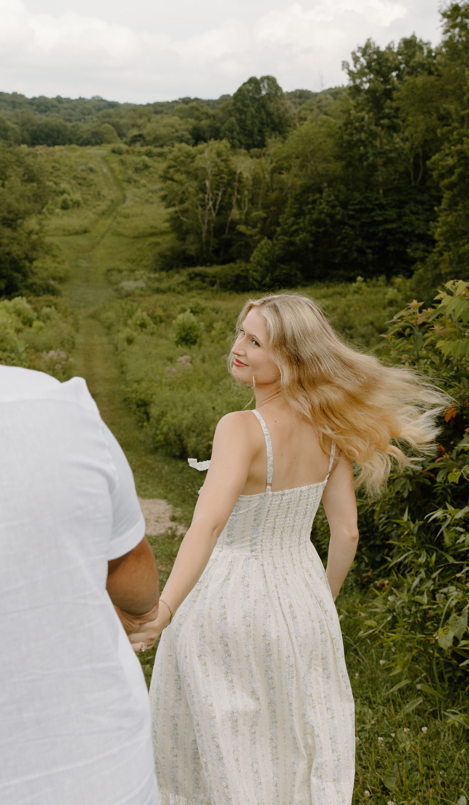 A figure in a flowing white sundress twirls through a lush green summer cuyahoga falls meadow on a sunny afternoon.