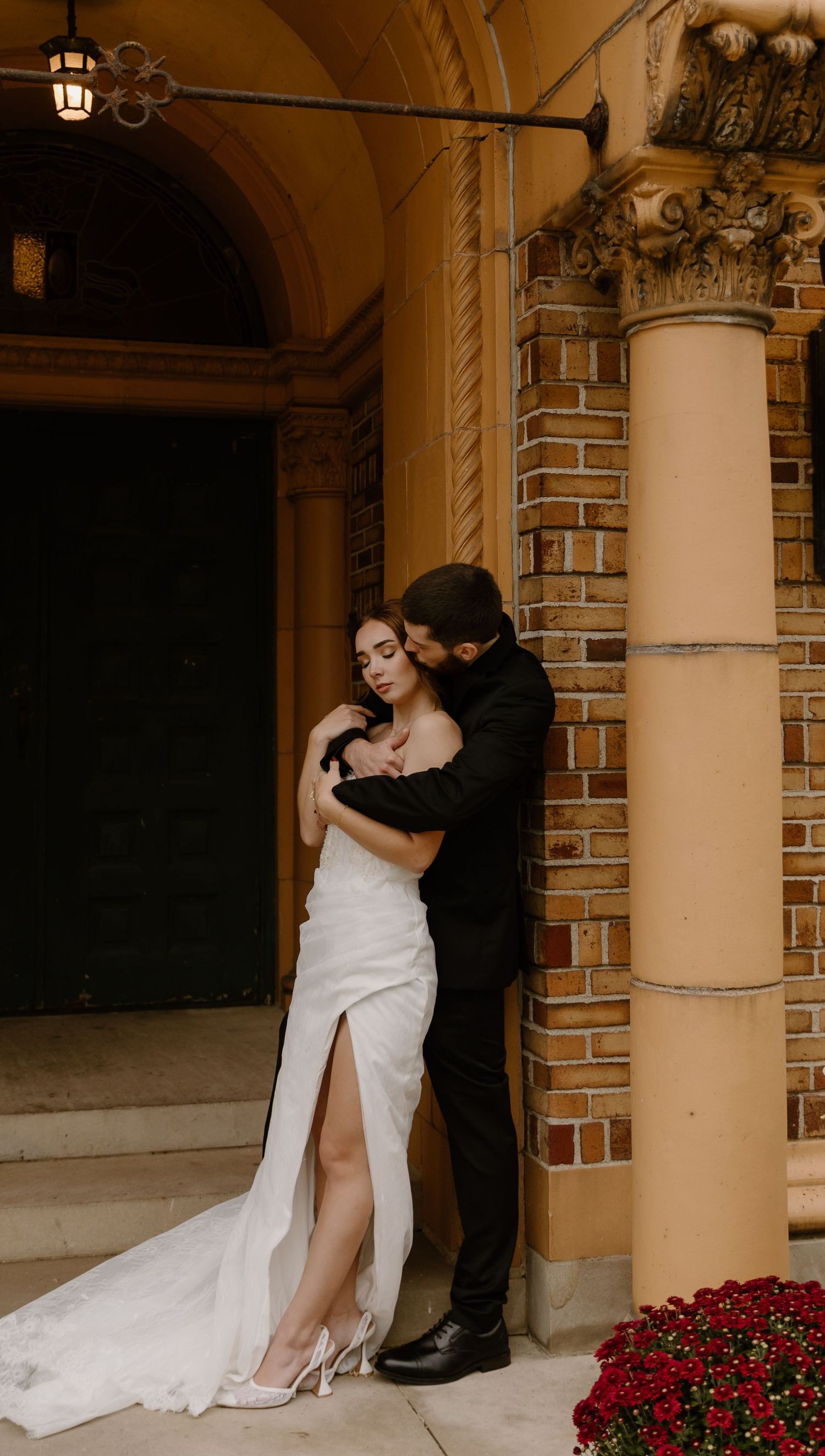 Romantic elopement moment captured outdoors with an intimate couple against scenic architecture, featuring vibrant red flowers