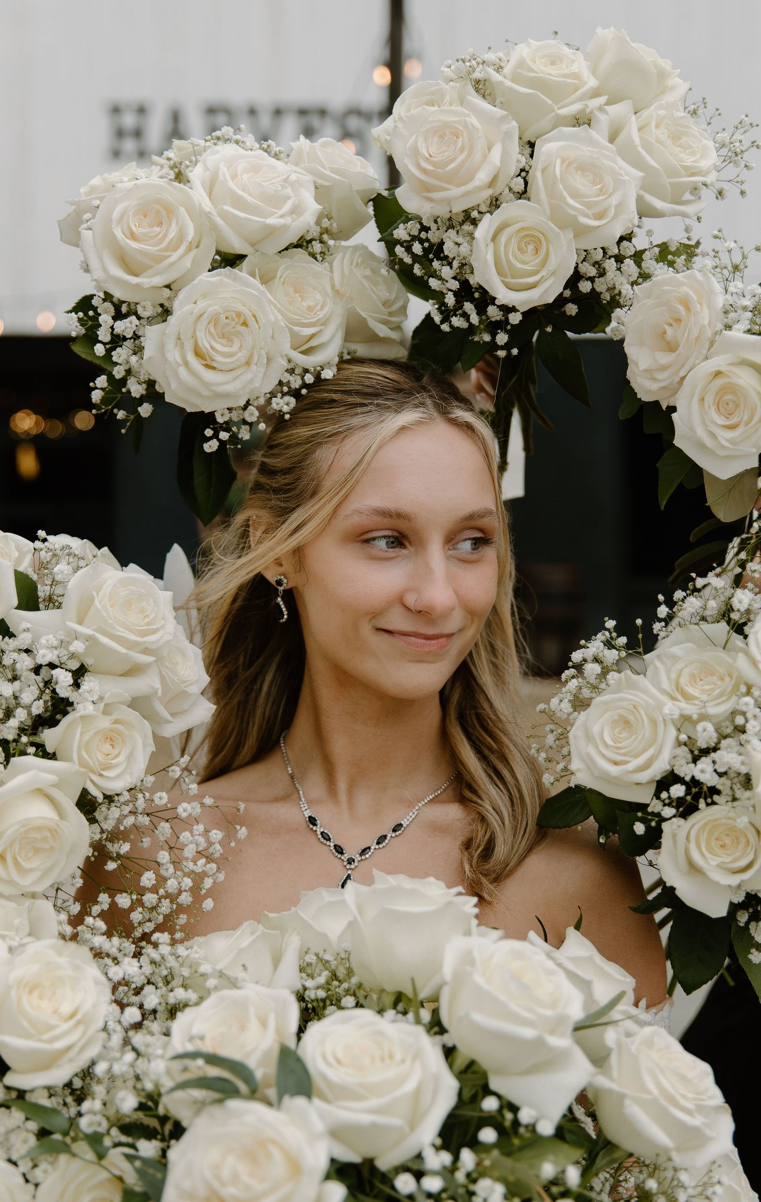 Smiling bride framed by beautiful white roses and baby's breath floral arch with sapphire necklace.