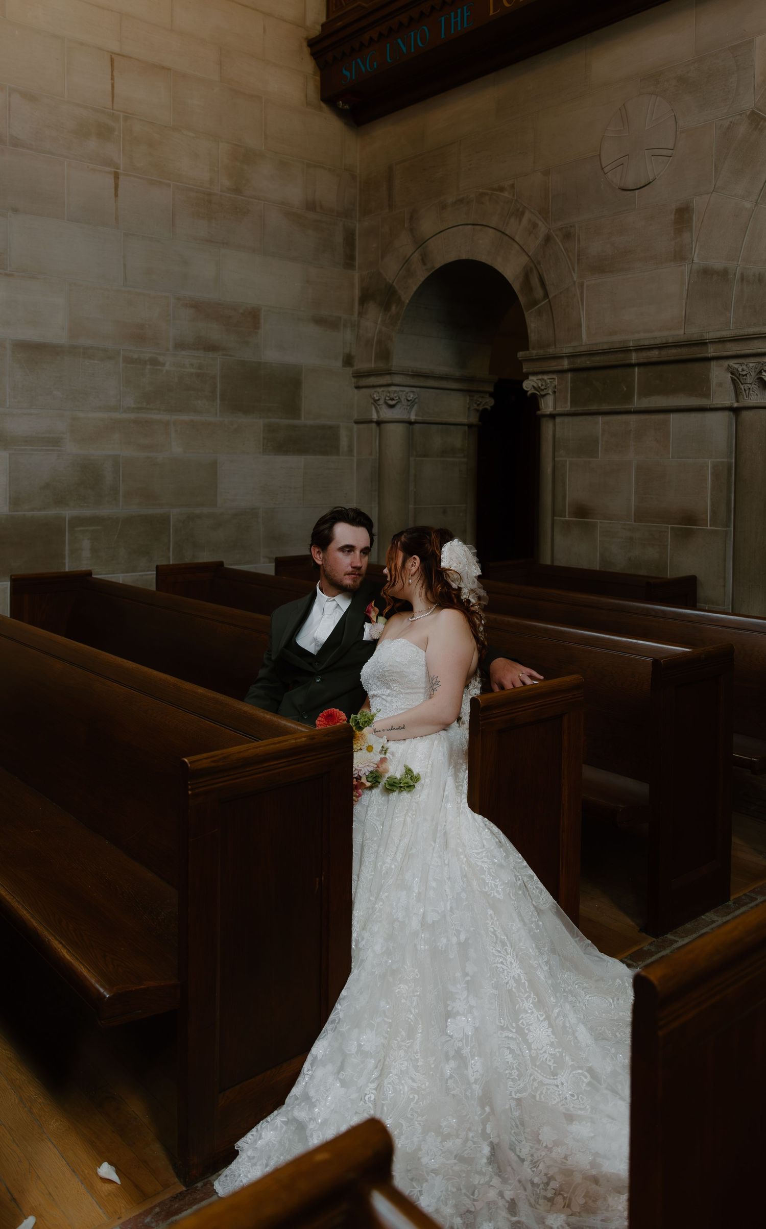 Bride and groom share a romantic moment among wooden church pews in a stone chapel on their wedding day.