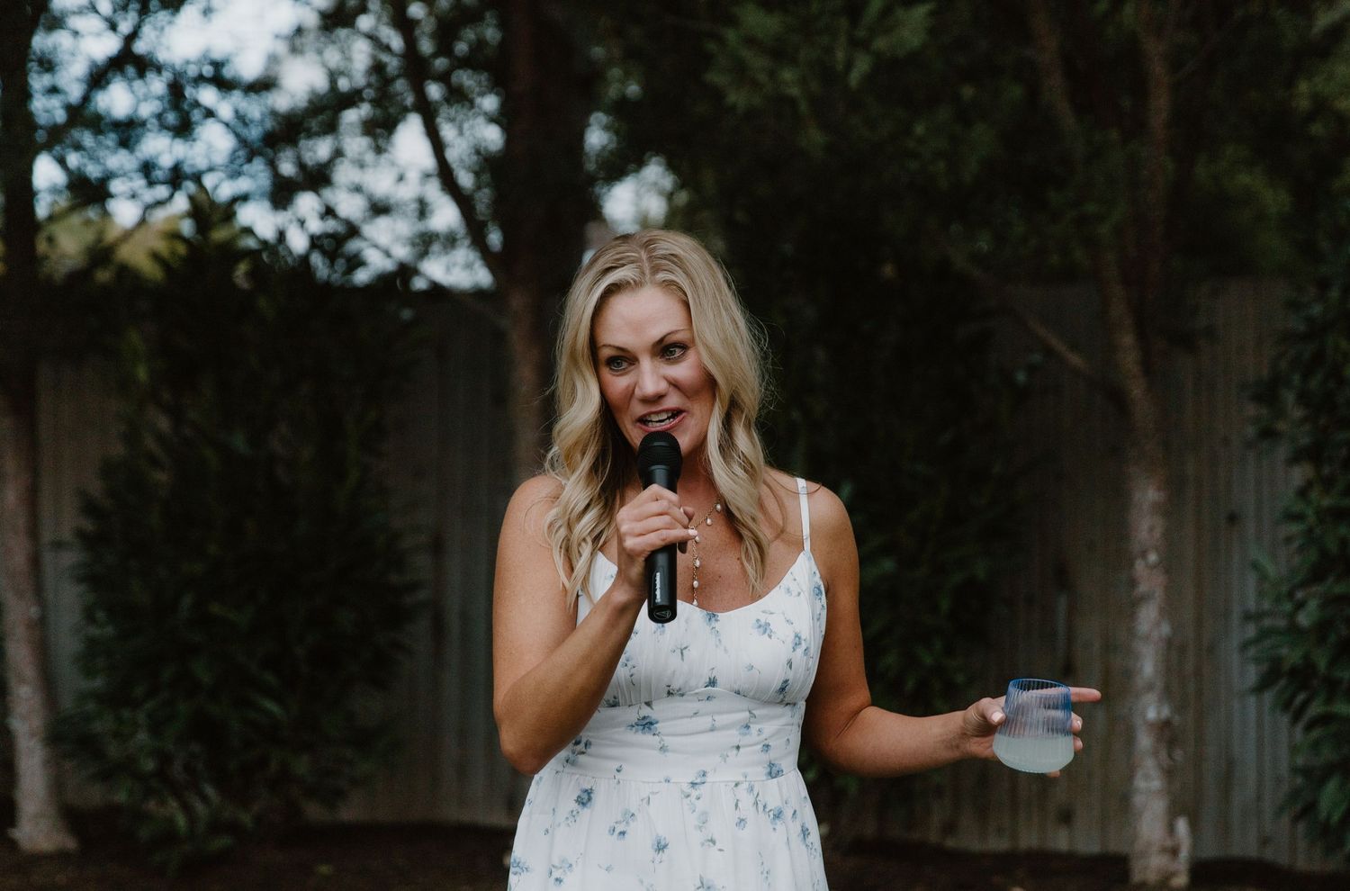 A person in a floral dress speaking into a microphone during an outdoor event.