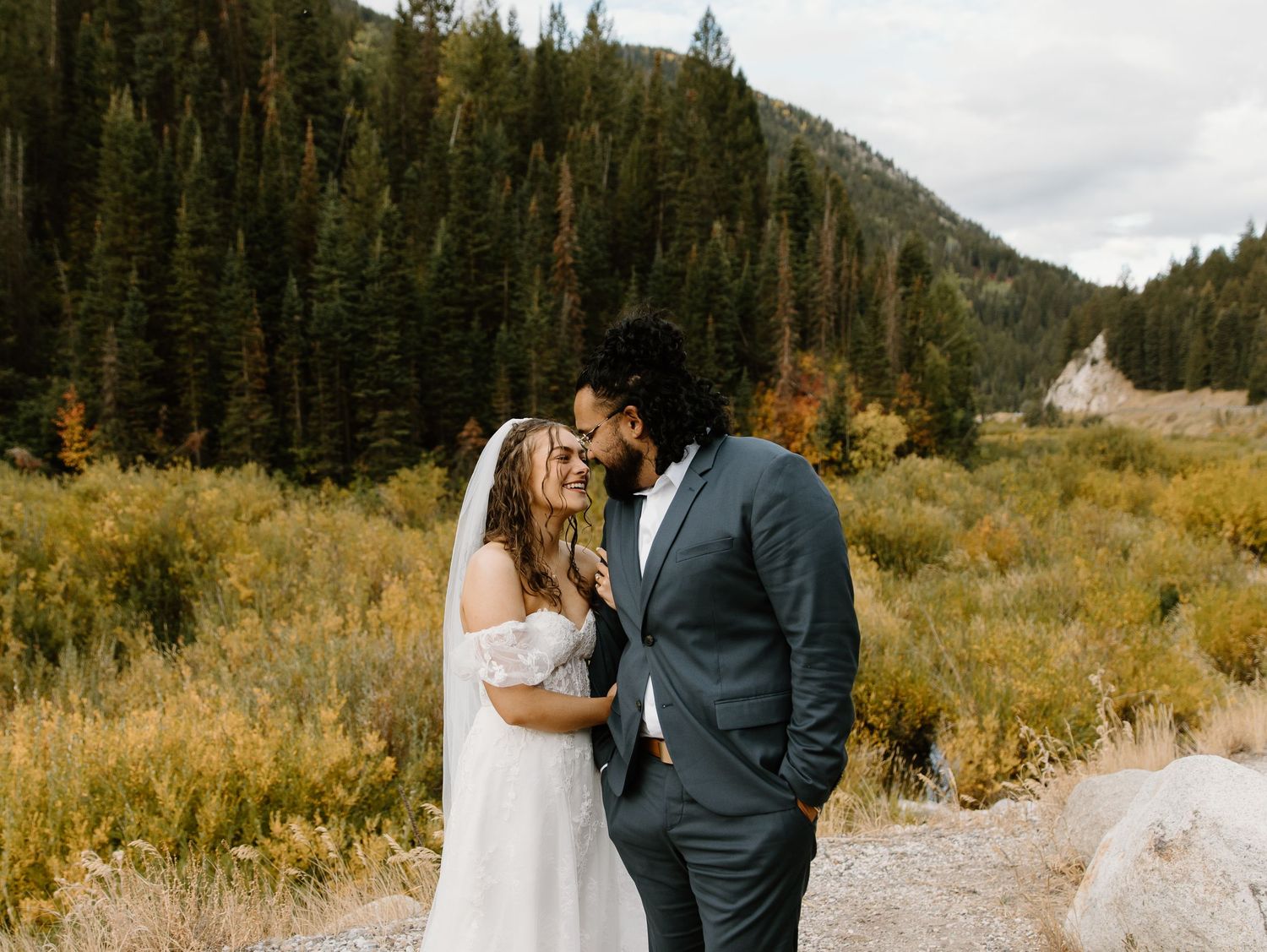 A couple embraces during their wedding photos in a scenic mountain landscape with golden autumn colors.