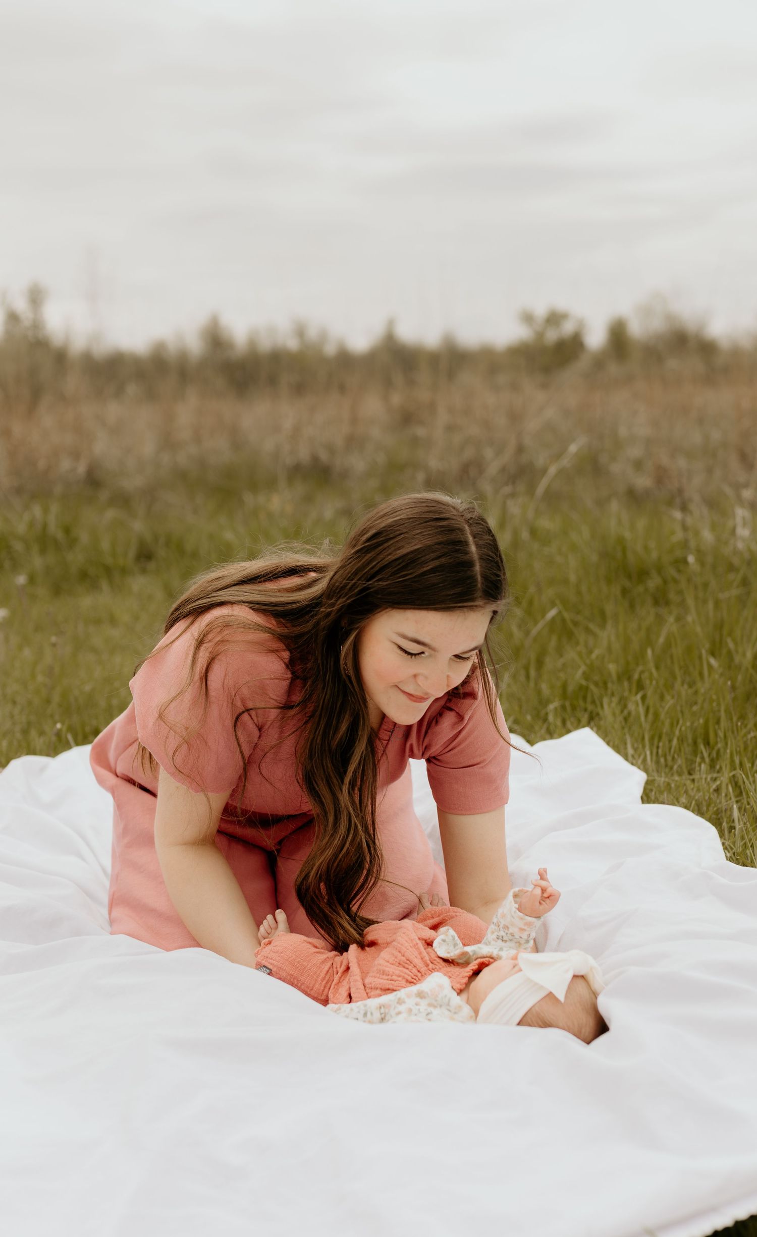 Someone in a coral dress rests on a white blanket in a sunny meadow while writing or journaling on a summer day.