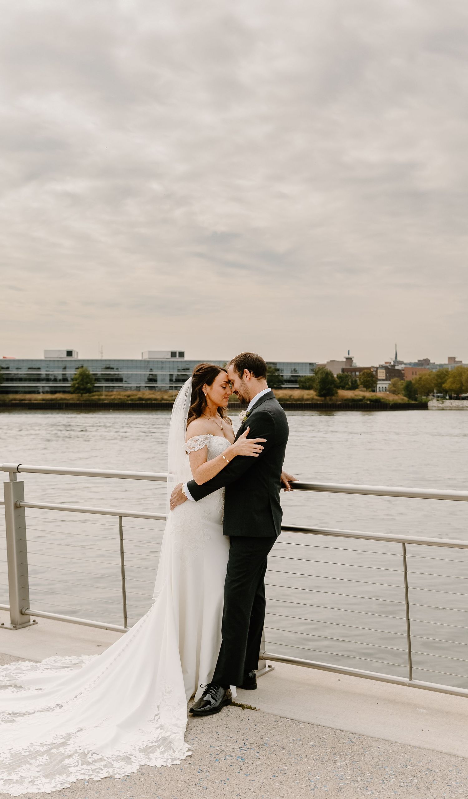 Newlyweds share an intimate moment on a waterfront terrace under cloudy skies.