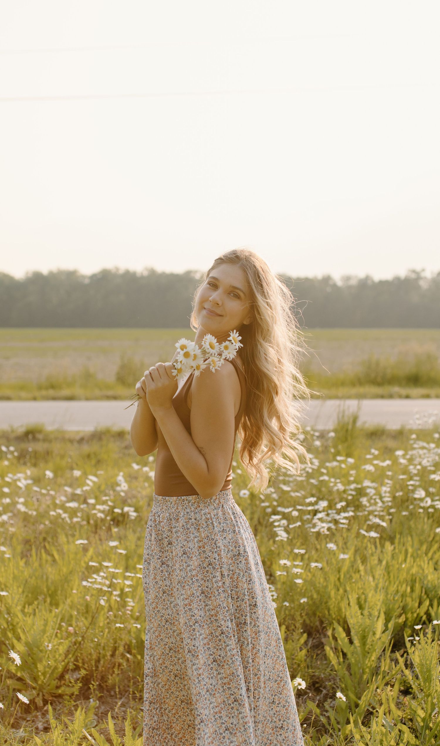 A figure in a floral dress standing in a sunlit meadow of wildflowers during golden hour.