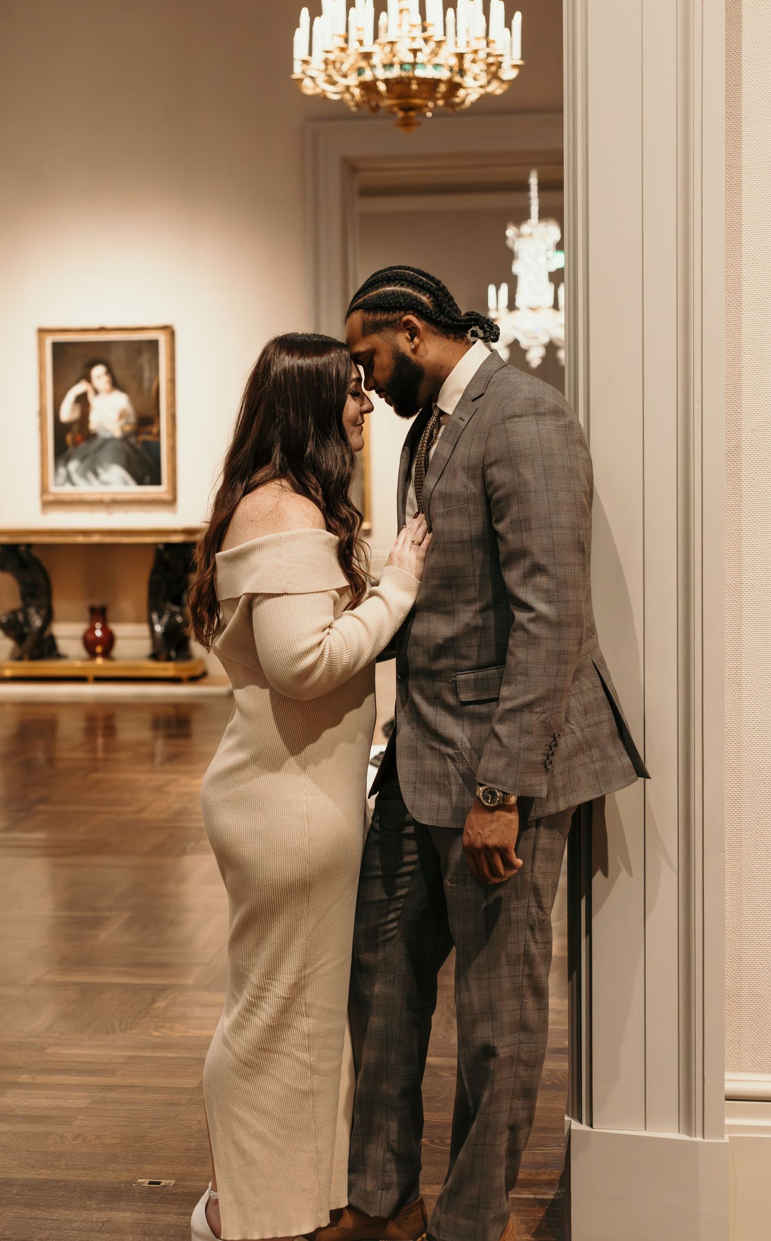 Romantic couple sharing an intimate moment under an elegant chandelier in a museum gallery.