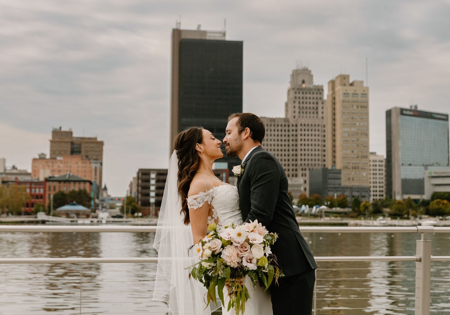 A couple shares romantic moments by the waterfront with the city skyline in the background.