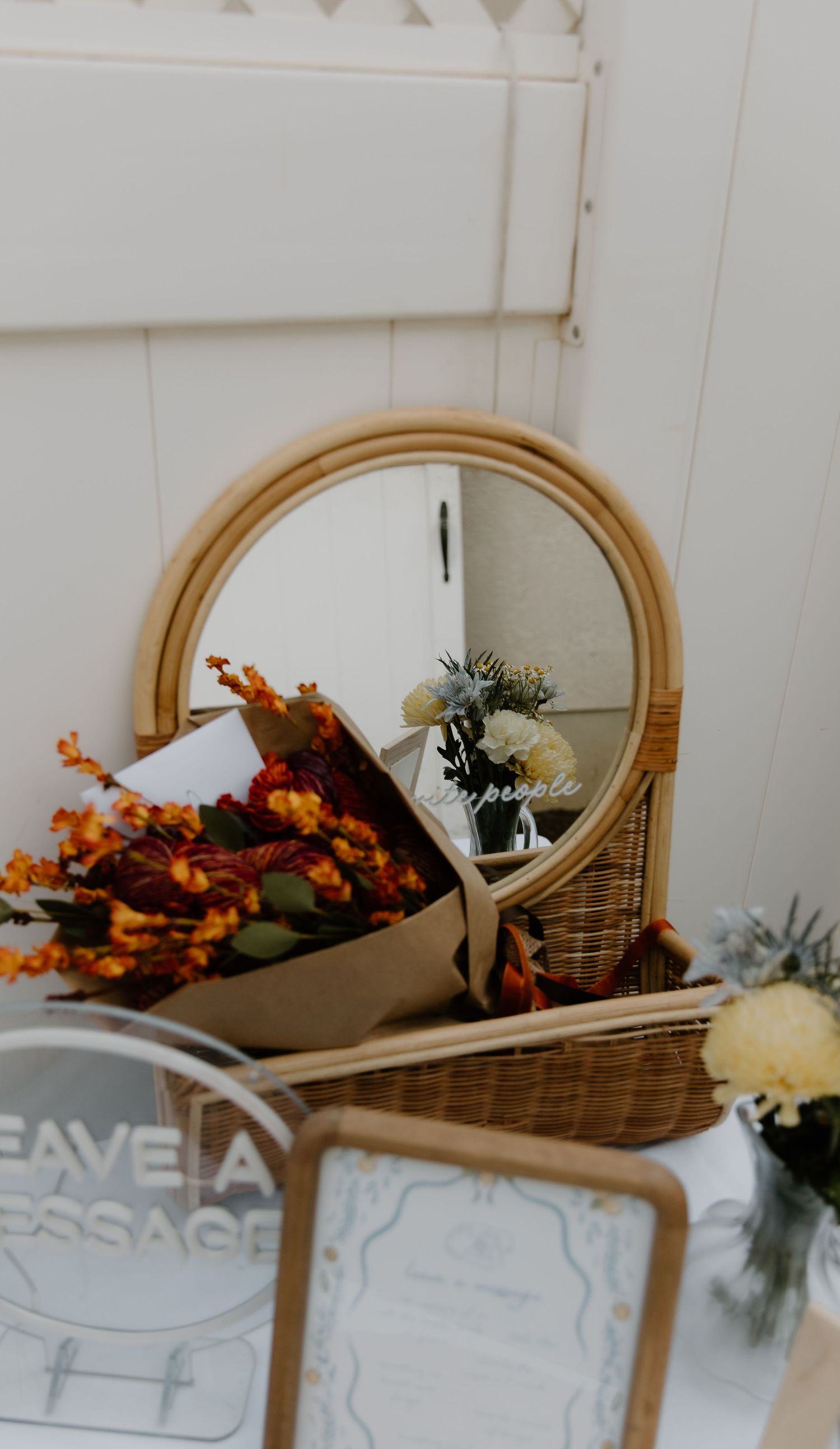 Decorative mirror and floral arrangements displayed against a white wall with autumn-colored flowers.