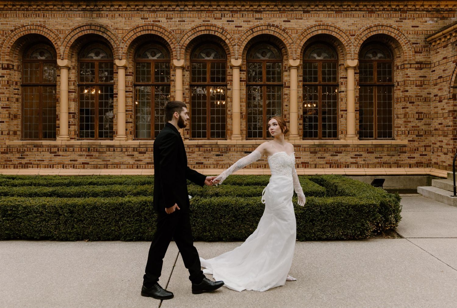 Elegant elopement couple walks along Nazareth Hall building with arched windows.