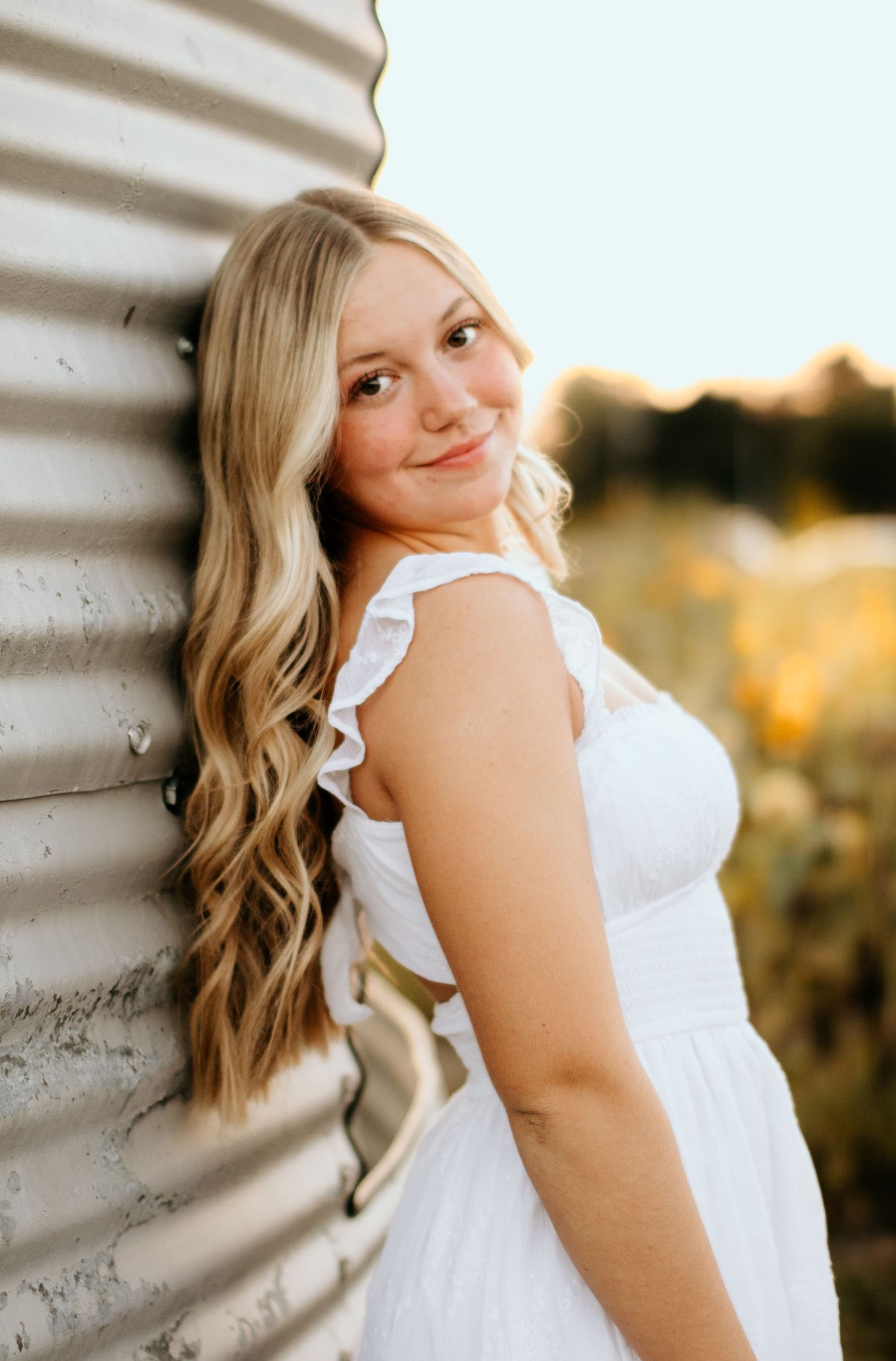 Portrait of a person in a white ruffled dress leaning against a wall at sunset.