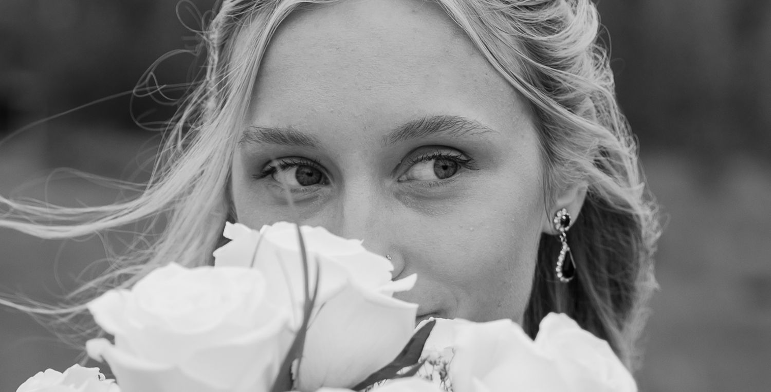 Black and white close-up of a blonde bride holding white roses near her face, showcasing elegant earrings.
