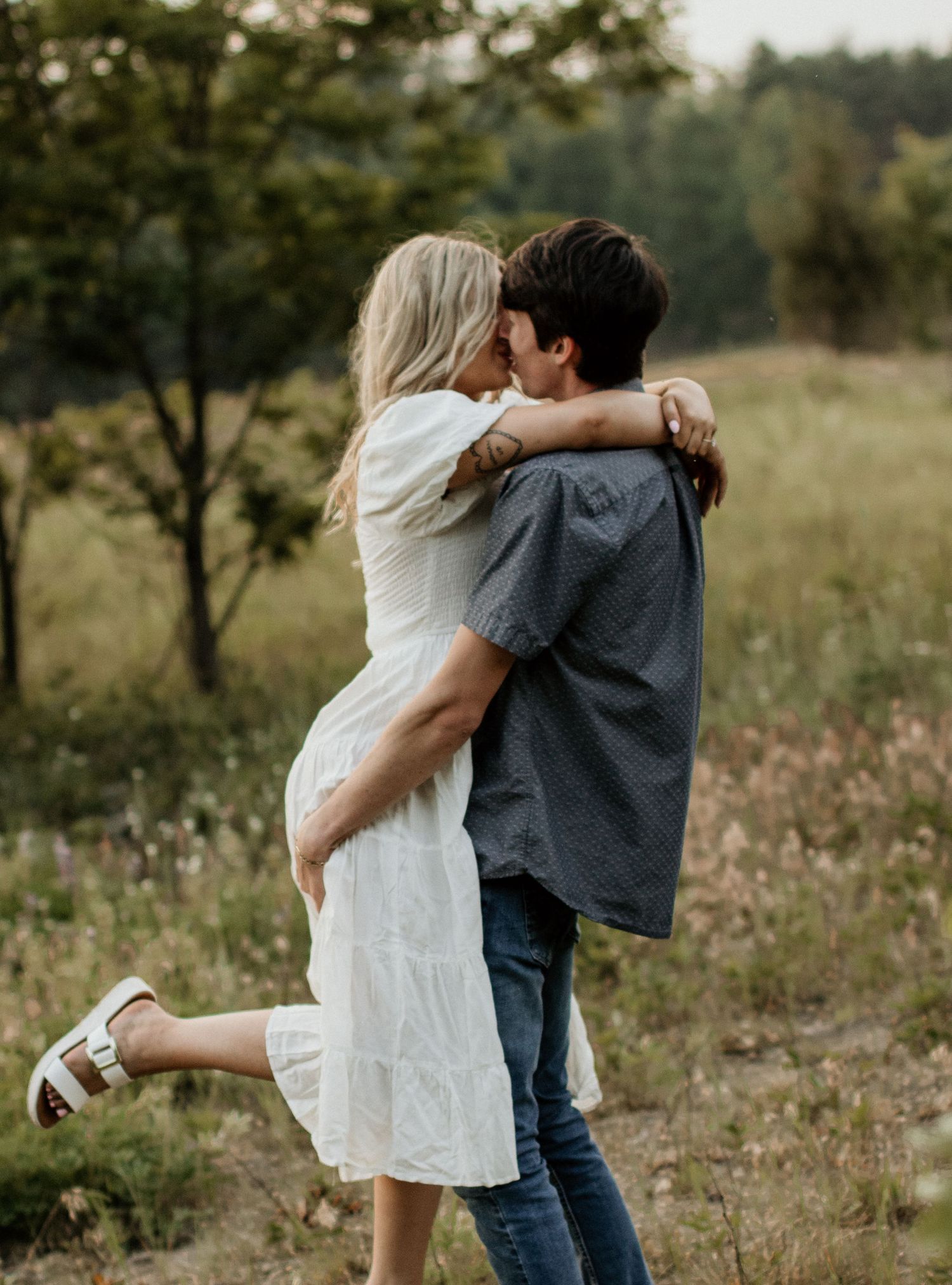 A couple embraces in a flowery field, with her feet lifted off the ground.