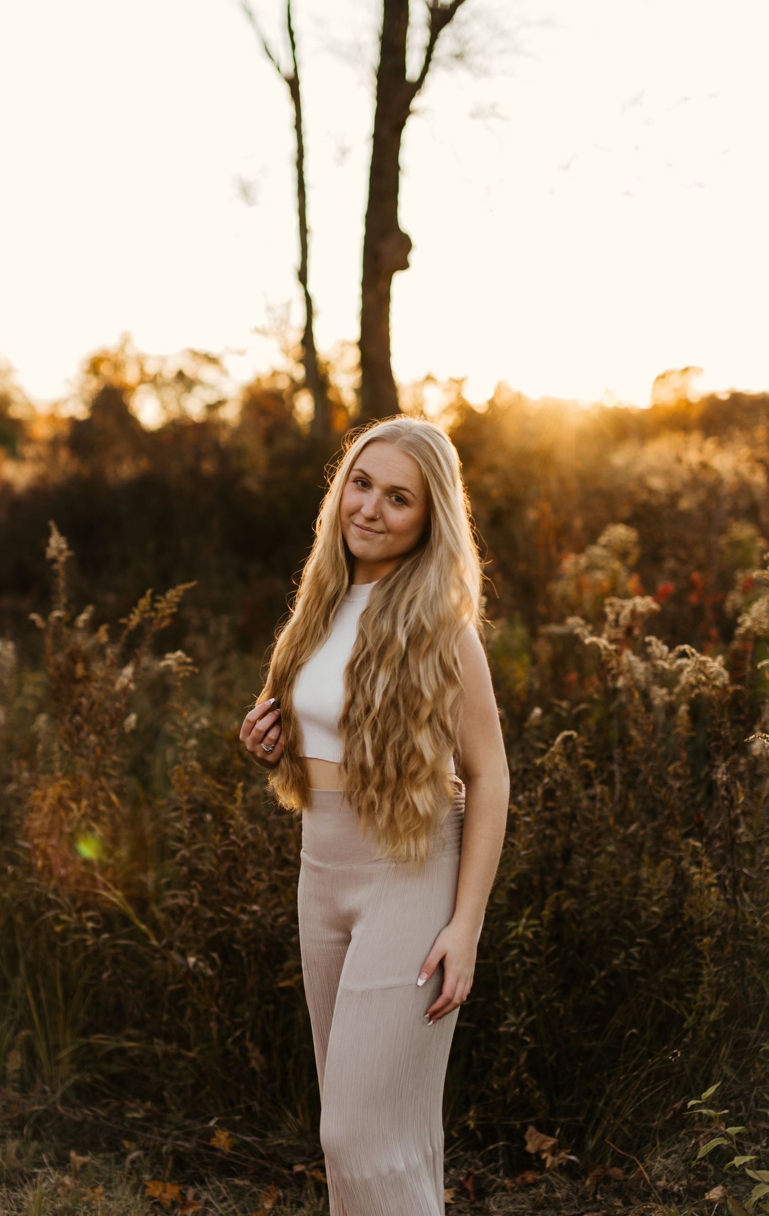 Sunset portrait in a field with golden light streaming through wild grasses and trees.