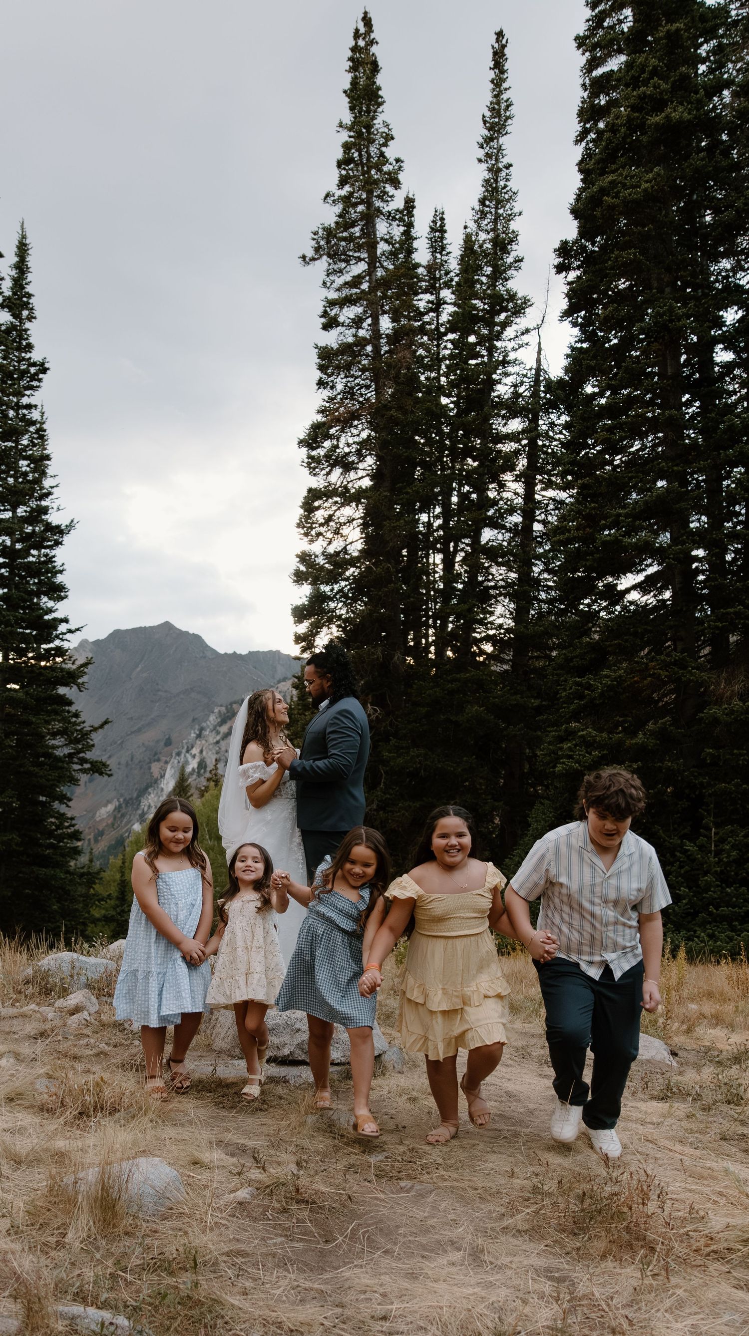 Wedding party in casual attire walking and laughing together on a mountain trail.
