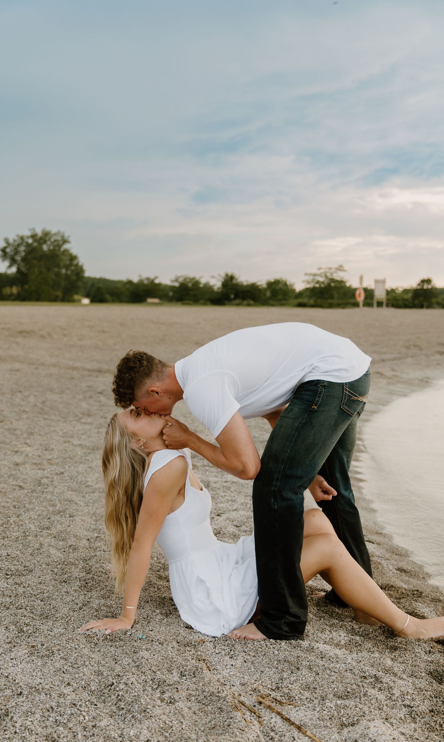 A romantic moment captured between two people on a sandy beach during sunset with soft cloudy skies in the background in Northwest Ohio.