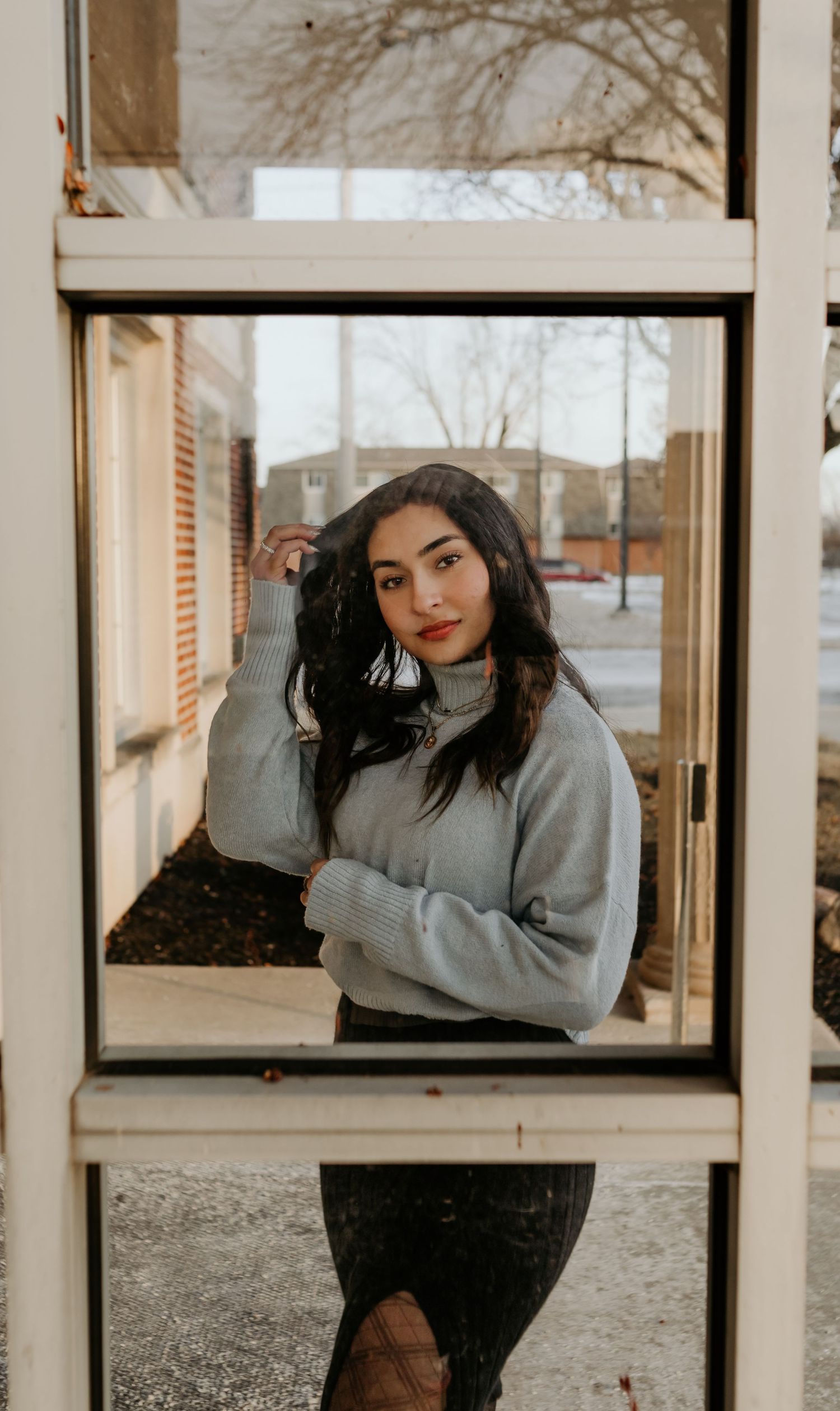 Person in grey sweater poses near window in casual winter attire.