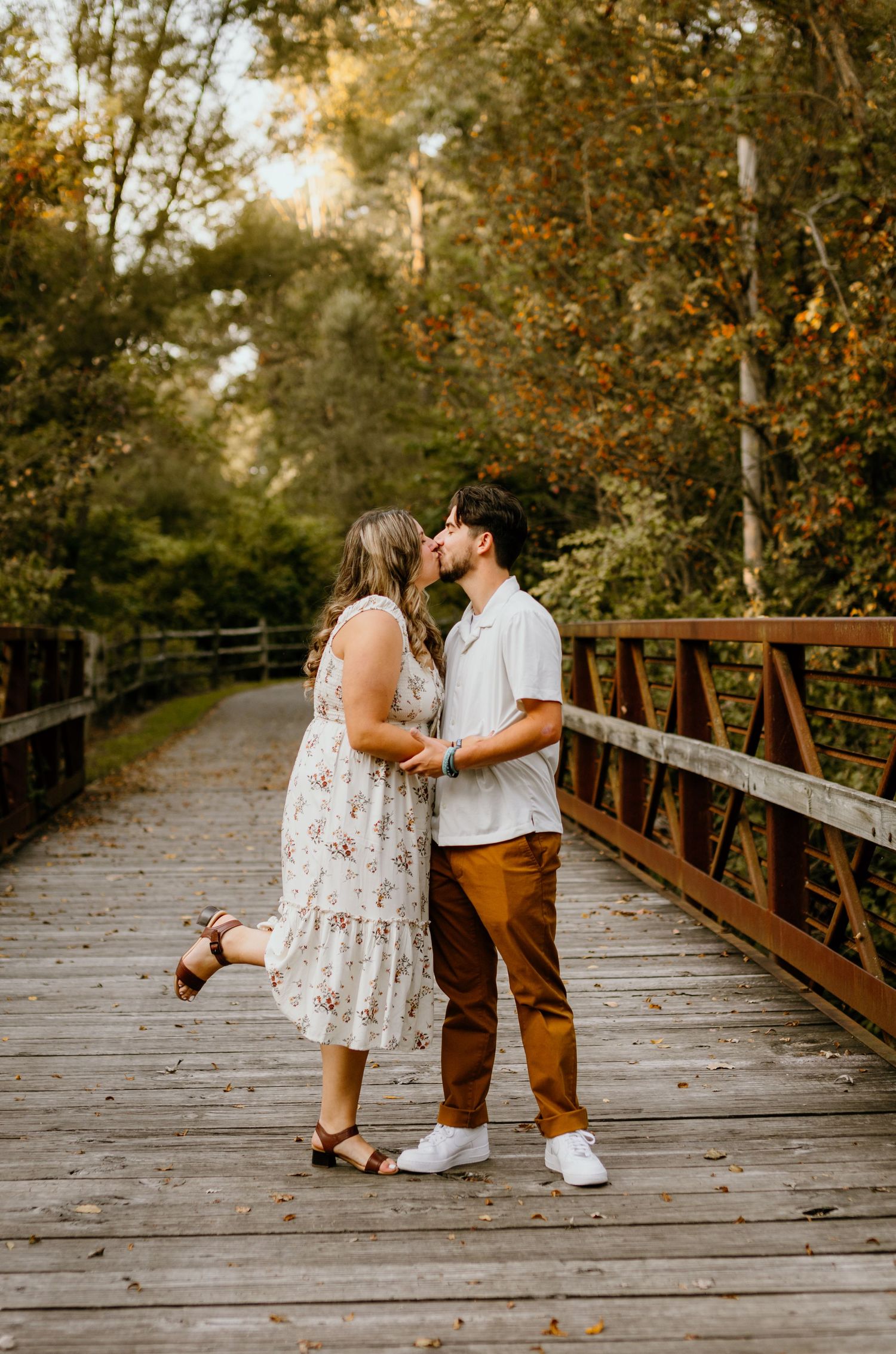 A romantic couple embraces on a wooden bridge during golden hour.