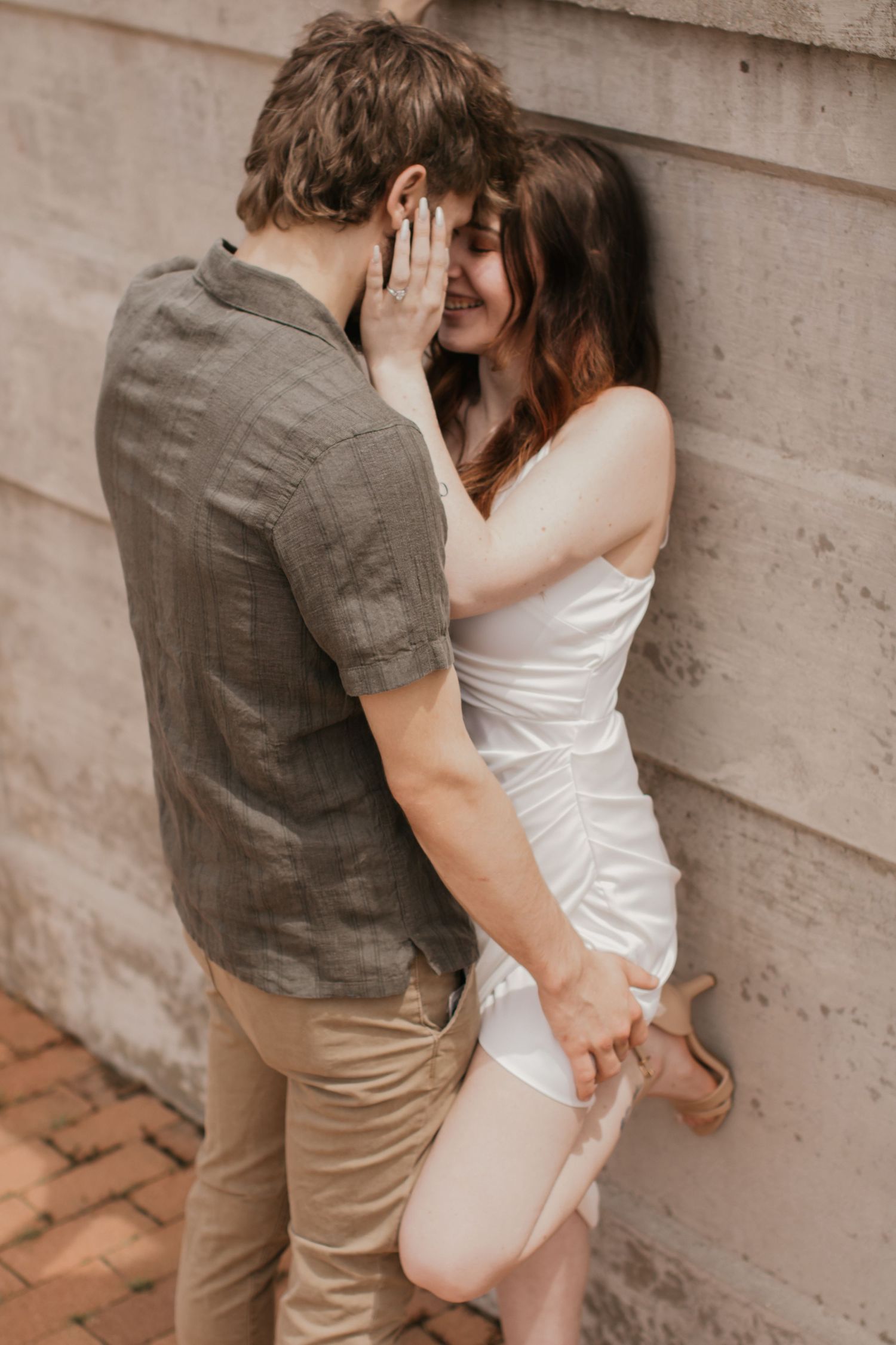 An intimate moment between a couple against a concrete wall, her in white and him in gray.