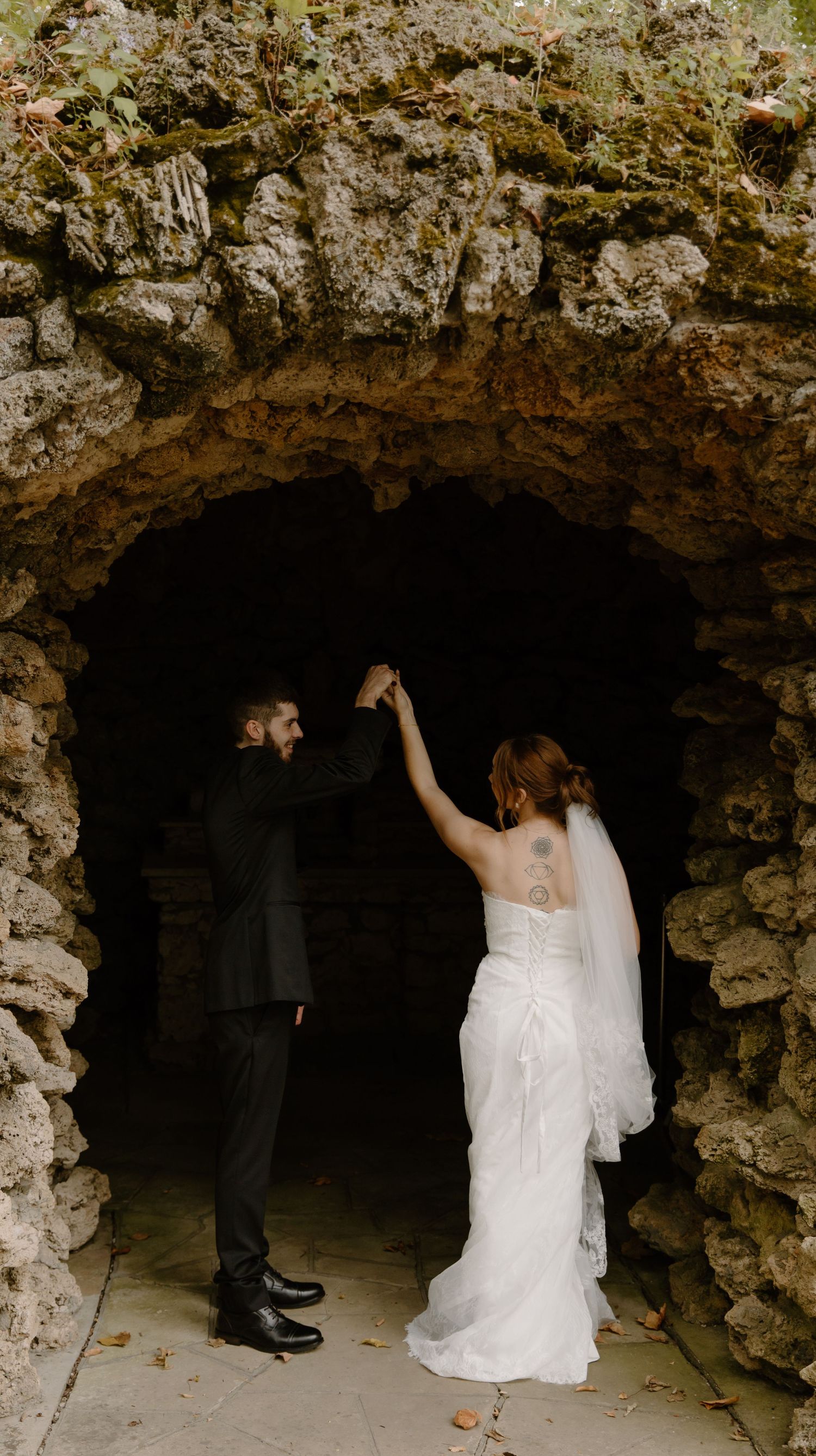 Elopement couple poses artistically in a rustic stone grotto or cave entrance for a romantic photo series.
