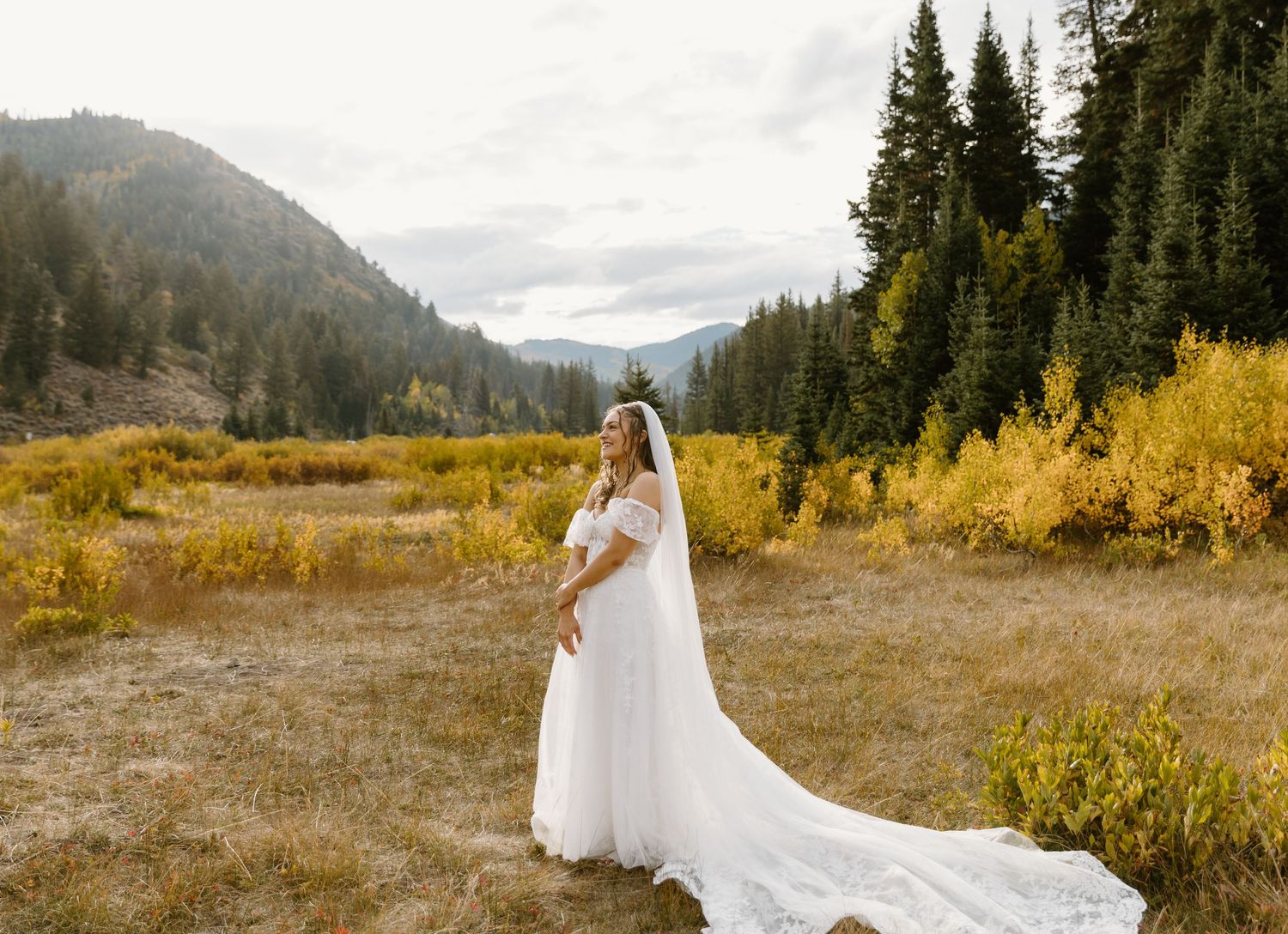 A flowing white dress billows in the mountain breeze against a backdrop of evergreen forest and autumn colors.