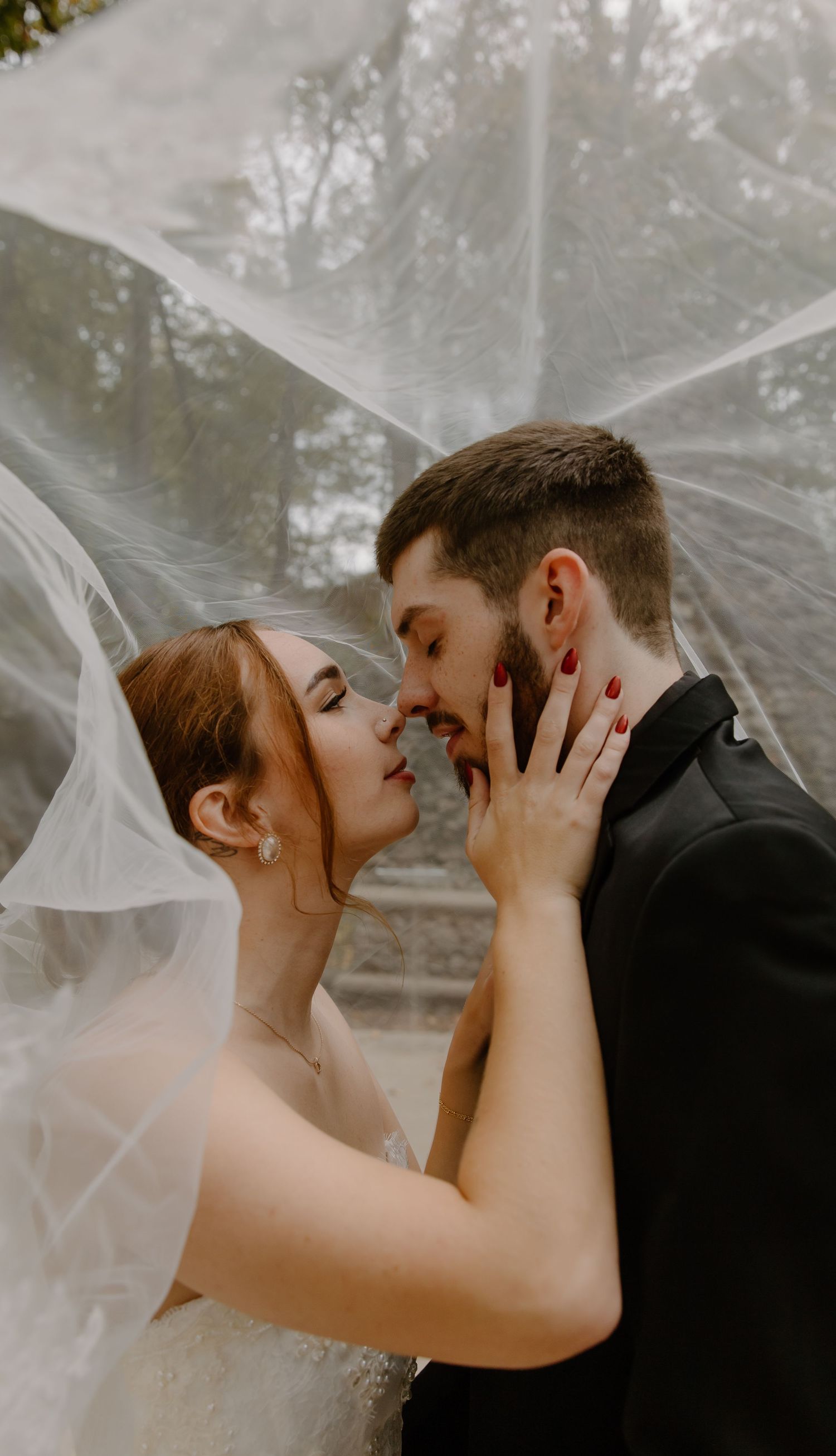 Romantic wedding couple shares an intimate kiss outdoors with flowing veil and moody lighting.