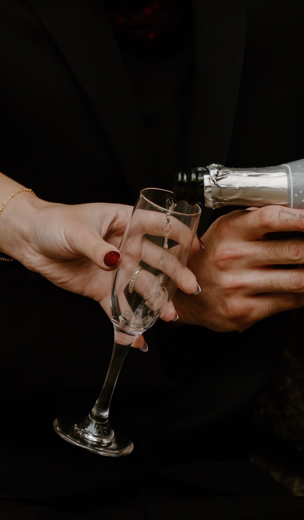 Two hands toasting with champagne glasses against a dark background in a dramatic lighting setup during an elopement.