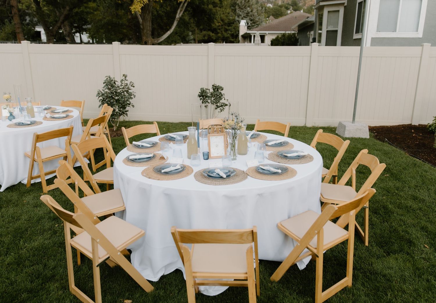 An elegant outdoor wedding reception setup with white tablecloths and wooden chairs.